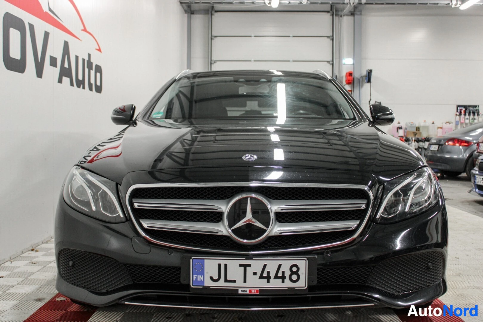 Edestä: Musta auto edestä kuvattuna sisätiloissa, rekisterikilpi