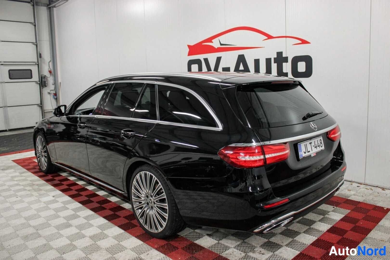 Takaviisto: Musta farmariauto takaa ja oikealta sivulta kuvattuna sisätiloissa, OV-Auto-logo taustalla. Autossa on kattokaiteet ja monipuoliset kevytmetallivanteet.