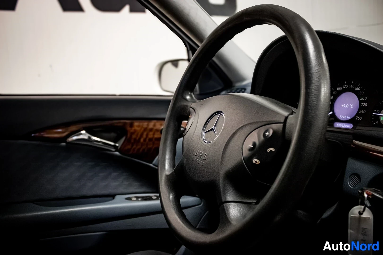 Ohjaamo: Sisätilakuva, jossa näkyy auton ohjauspyörä keskikonsoliin päin katsottuna. Ohjauspyörässä on näppäimiä ja Mercedes-Benz-logo.
