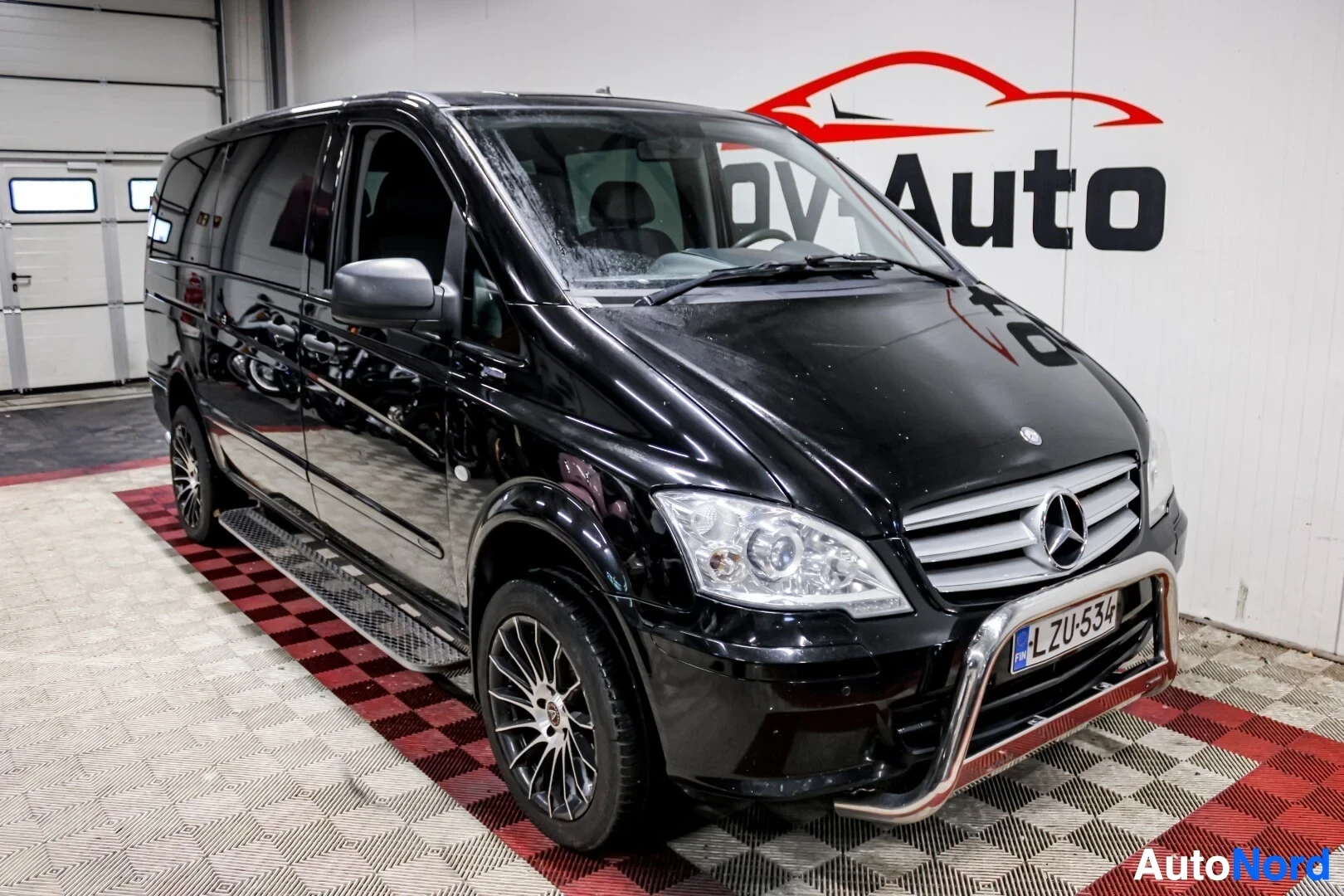 Etuviisto, nokka vasemmalle: Musta Mercedes-Benz Vito -pakettiauto edestä ja vasemmalta sivulta kuvattuna. Ajoneuvossa on krominen puskurinsuojus ja monipuolaiset kevytmetallivante