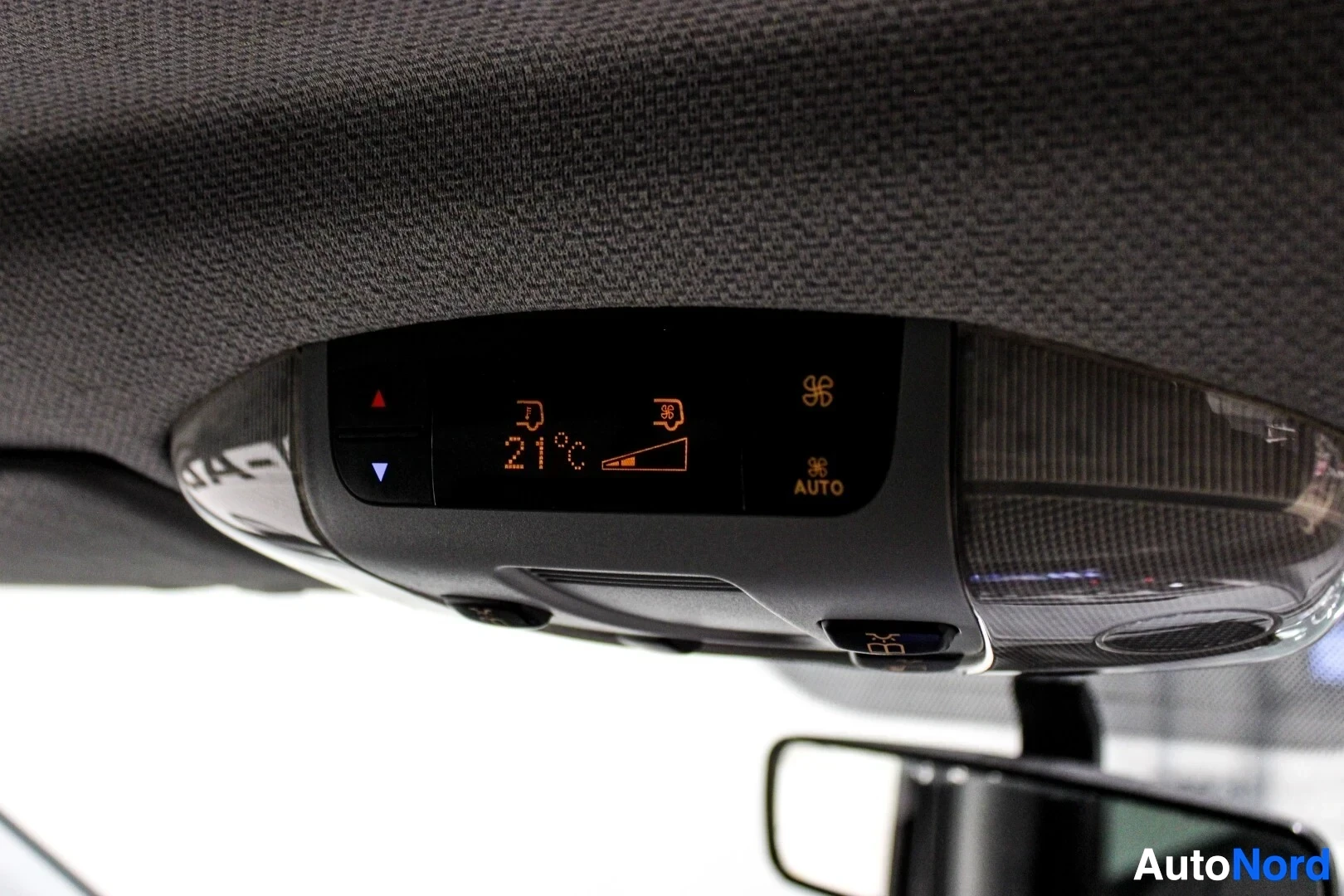 Yksityiskohta: Lähikuva auton kattoon asennetusta digitaalisesta ilmastointiohjauspaneelista. Näytöllä lukee "21°C" ja "AUTO". Paneelissa on myös puhaltimen ja lämpötilan säät