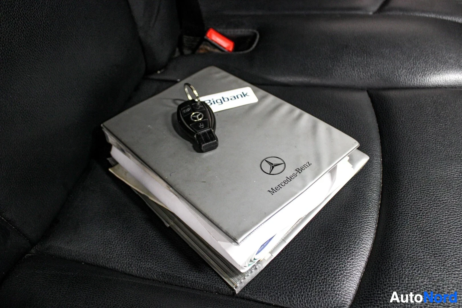 Yksityiskohta: Mustalla istuimella näkyy harmaa Mercedes-Benz-kansio, jonka päällä on avainnippu, jossa on Mercedes-Benz-logo ja Bigbank-avainperä.
