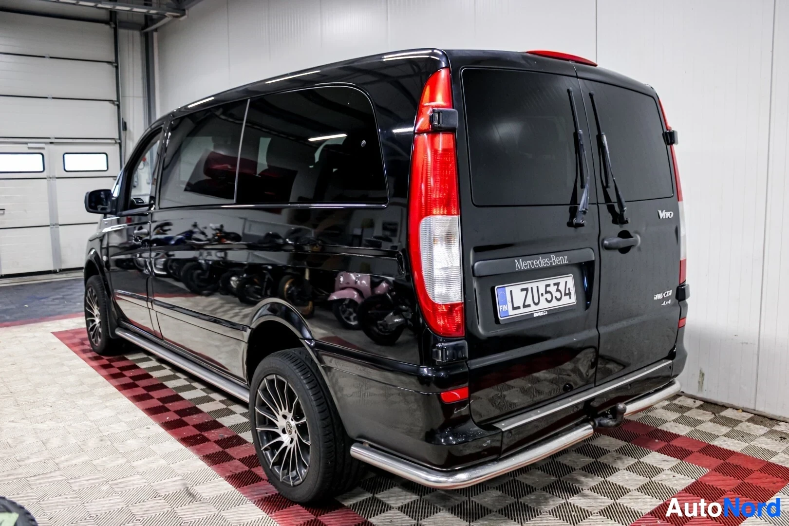 Takaviisto: Musta pakettiauto, jossa on tummennetut ikkunat ja vetokoukku, kuvattuna takavasemmalta viistosta. Takaosa näkyy, samoin kuin auton vasen kylki.