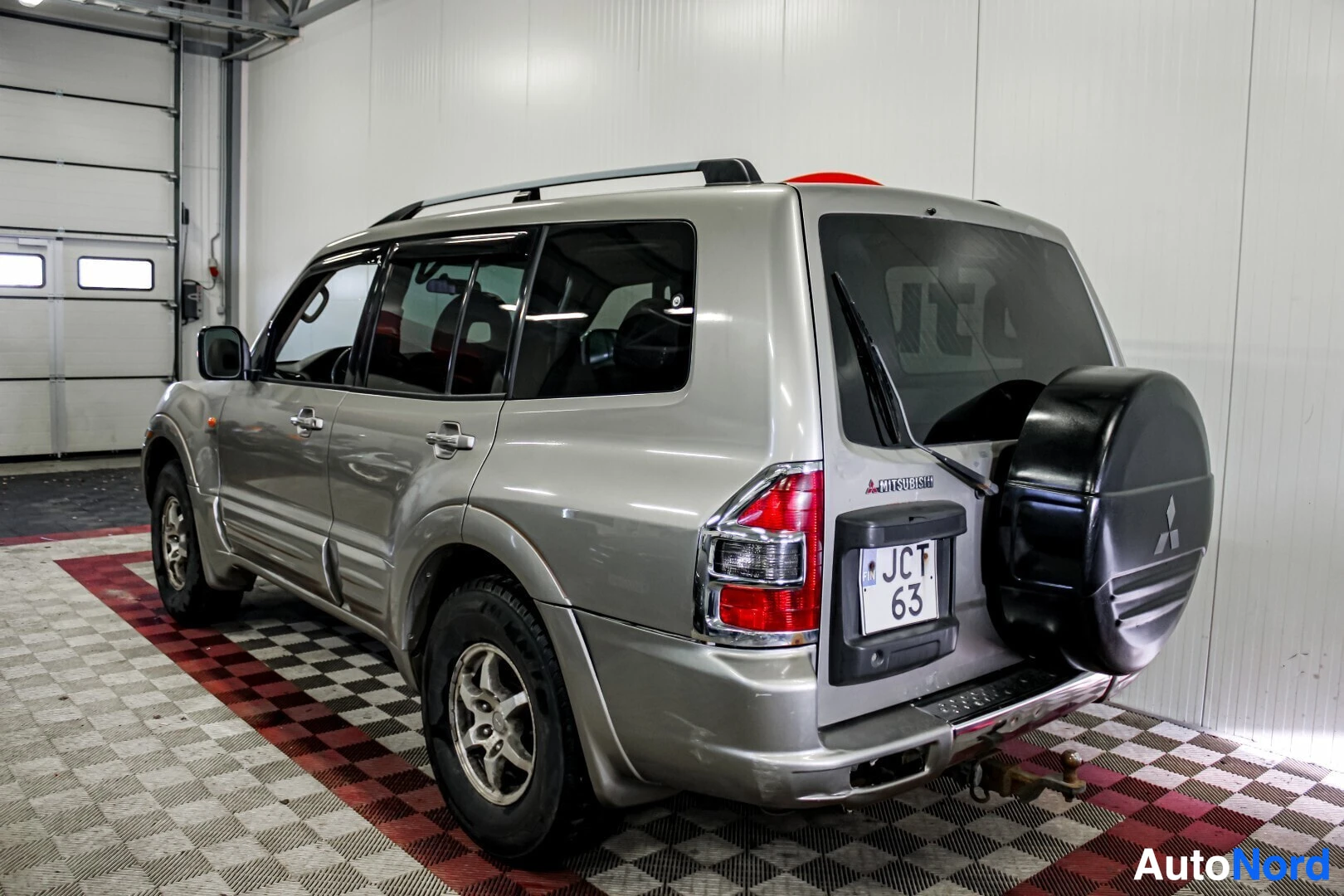 Takaviisto: Hopeanvärinen SUV-auto kuvattuna takavasemmalta. Rekisterikilpi "JCT 63" on näkyvissä. Auton takaluukussa on vararengas, ja katolla on kattokiskot. Takana näkyy