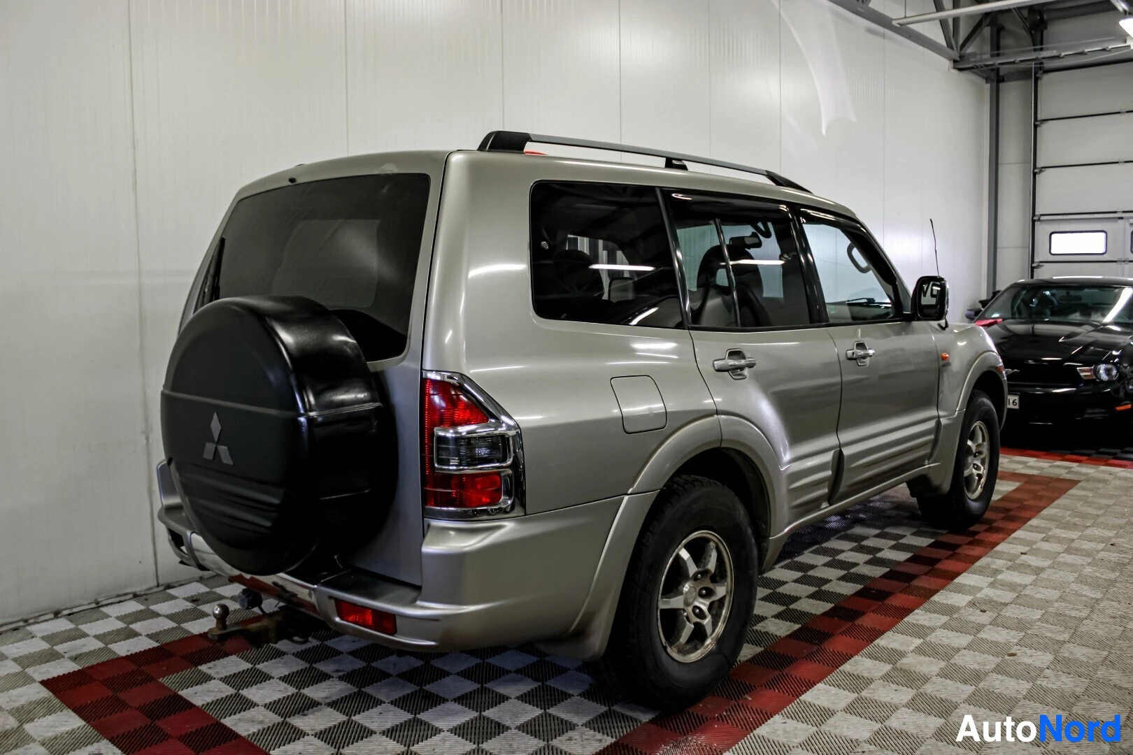 Takaviisto: Hopeanvärinen SUV-auto kuvattuna takaoikealta. Auton takaluukussa on vararengas. Oikealla takana näkyy osittain toinen tumma auto.