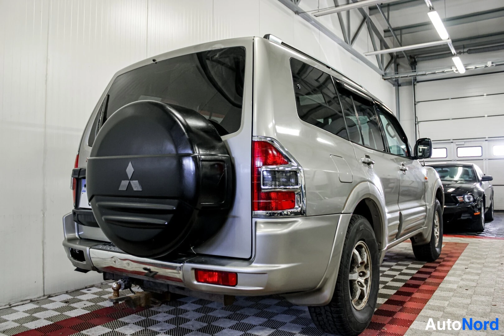 Takaviisto: Hopeanvärinen SUV-auto kuvattuna takaoikealta matalasta kuvakulmasta. Auton takaluukussa on vararengas, ja vetokoukku on näkyvissä. Oikealla taustalla näkyy toi