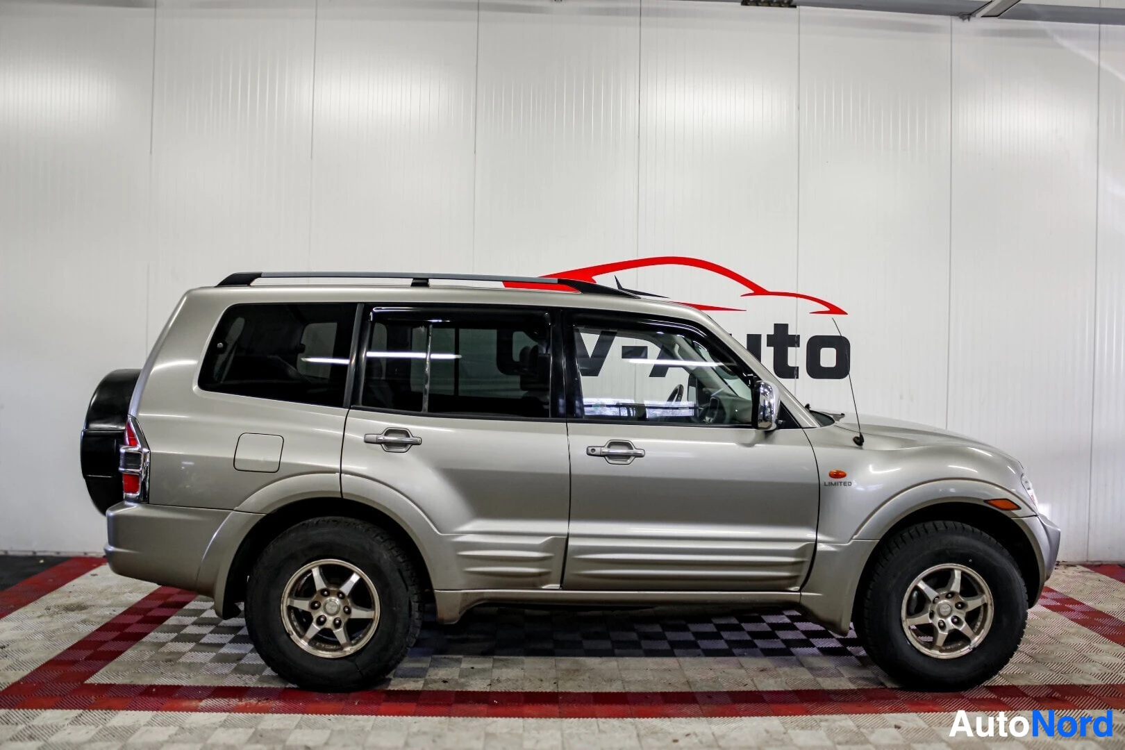 Sivulta: Hopeanvärinen SUV-auto kuvattuna suoraan sivulta. Auton sivuprofiili on selkeästi esillä. Katolla on kattokiskot, ja takaluukussa on vararengas.