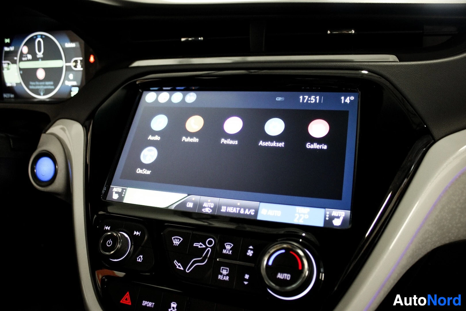 Ohjaamo: Auton infotainment-järjestelmän keskinäyttö, jossa on kuvakkeita eri toiminnoille ja ilmastoinnin säätimet sen alapuolella.