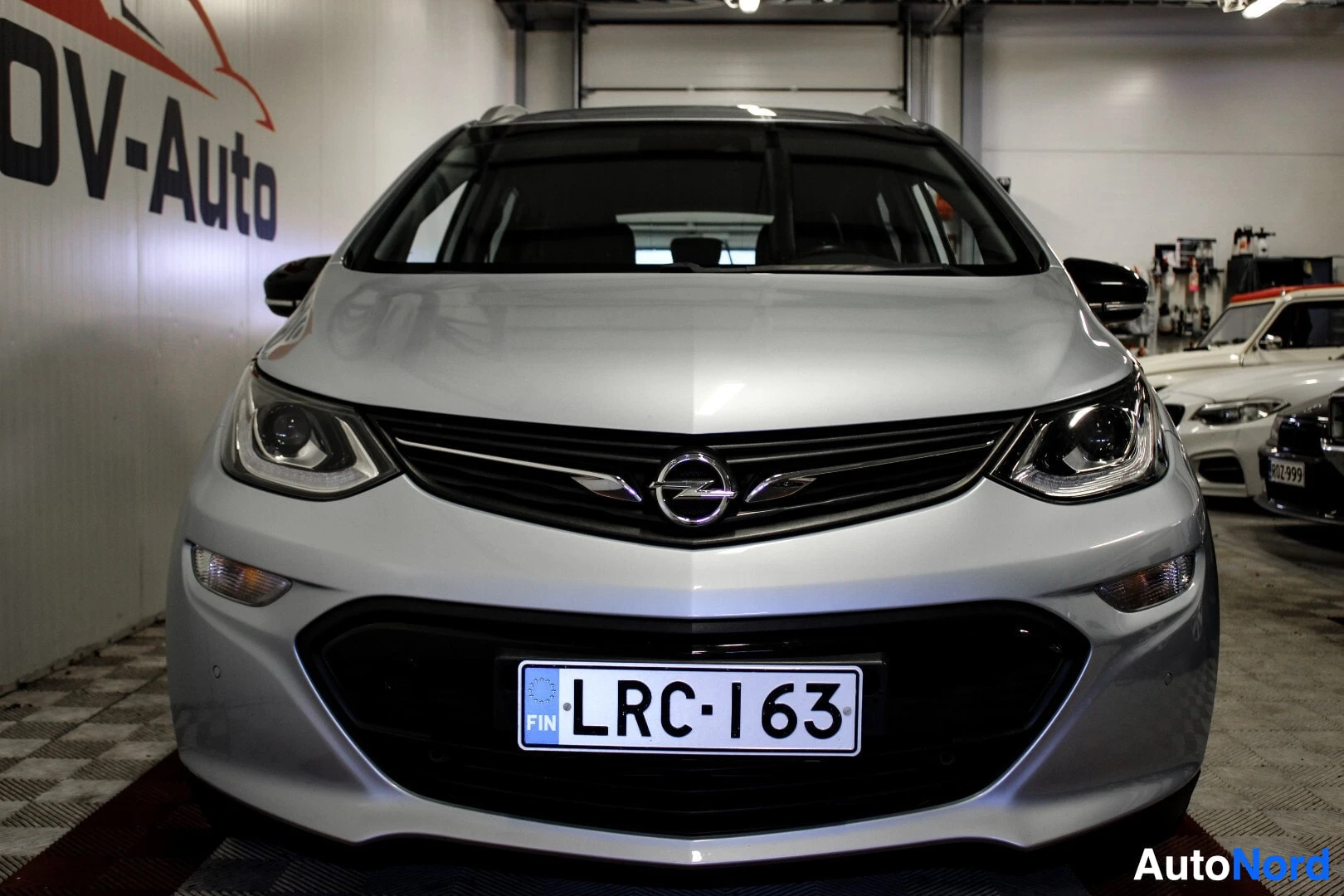 Edestä: Hopeanvärinen Opel Ampera-e edestä kuvattuna. Etusäleikkö, ajovalot, etupuskuri ja rekisterikilpi ovat selvästi näkyvissä.