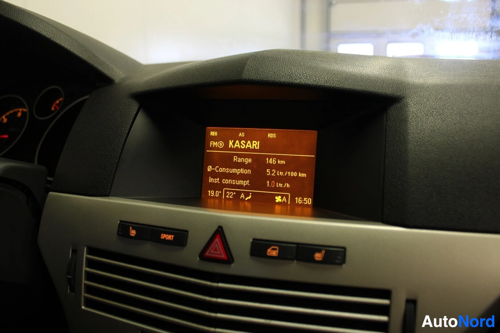 Yksityiskohta: Lähikuva auton kojelaudan näytöstä, jossa lukee 'FM0 KASARI', 'Range 146 km', '0-Consumption 5.2 Ltr./100 km', 'Inst. consumpt. 1.0 Ltr./h' ja '19.0° 22° A 16:5
