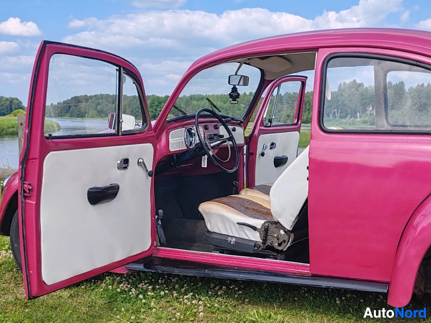Sivulta: Vaaleanpunainen kaksiovinen auto, jossa molemmat ovet ovat auki. Keskellä näkyy ohjauspyörä, kojelauta ja kuljettajan istuin. Istuimet ovat beige-valkoiset ja r