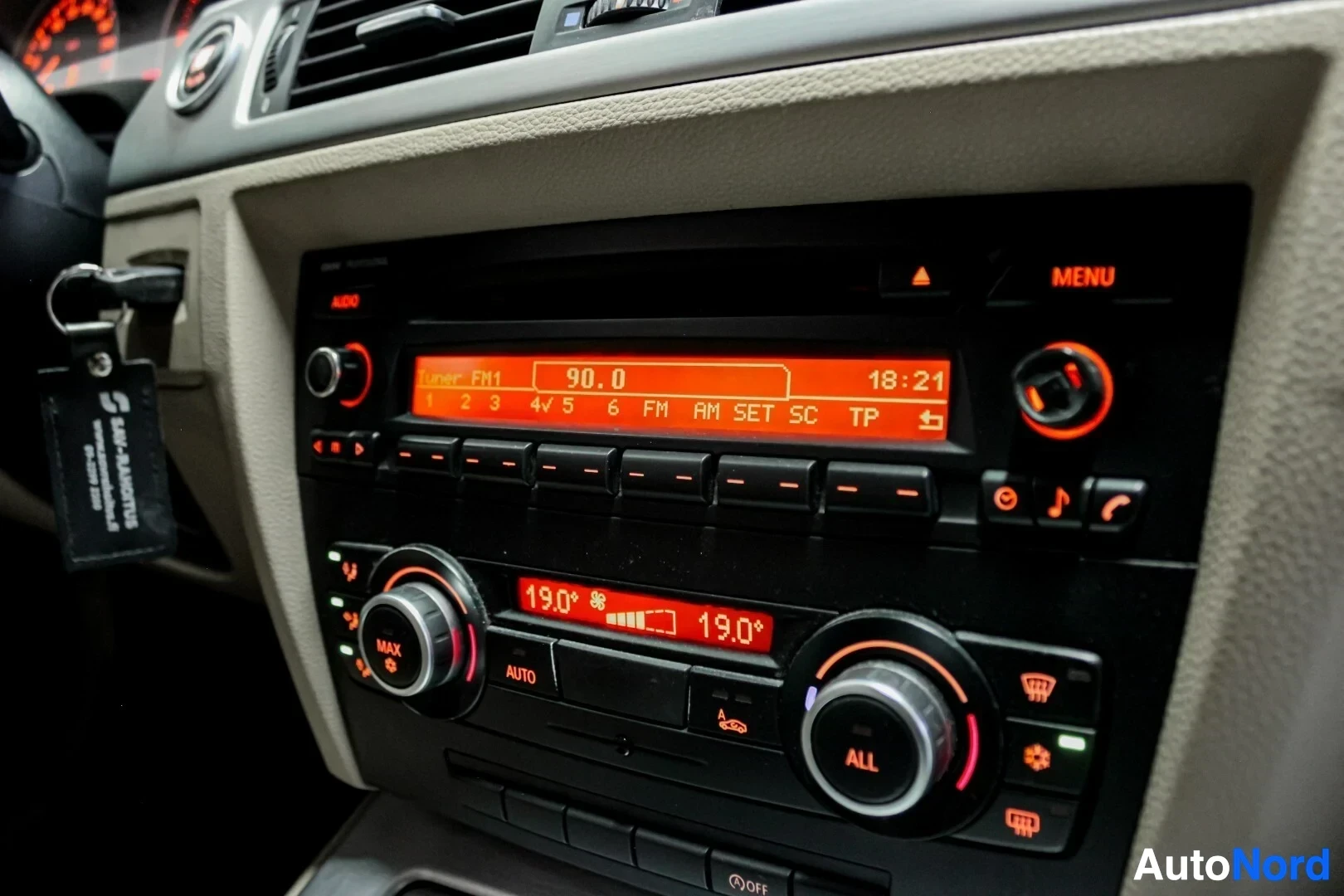 Yksityiskohta: Lähikuva auton keskikonsolin radio- ja ilmastointilaitteista. Radion näytöllä lukee "Tuner FM1 90.0" ja ilmastointilaitteen näytöllä "19.0" molemmilla puolilla.