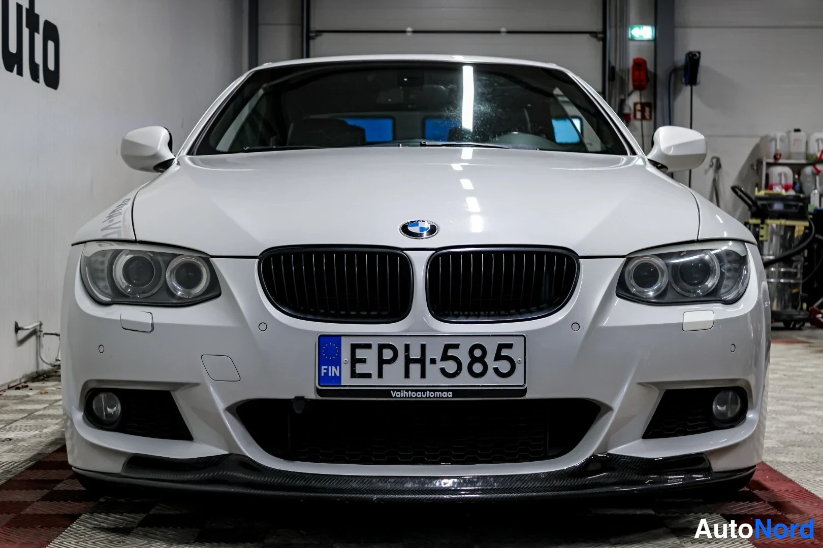 Edestä: Valkoisen BMW-henkilöauton etupää suoraan edestä kuvattuna; rekisterikilpi.