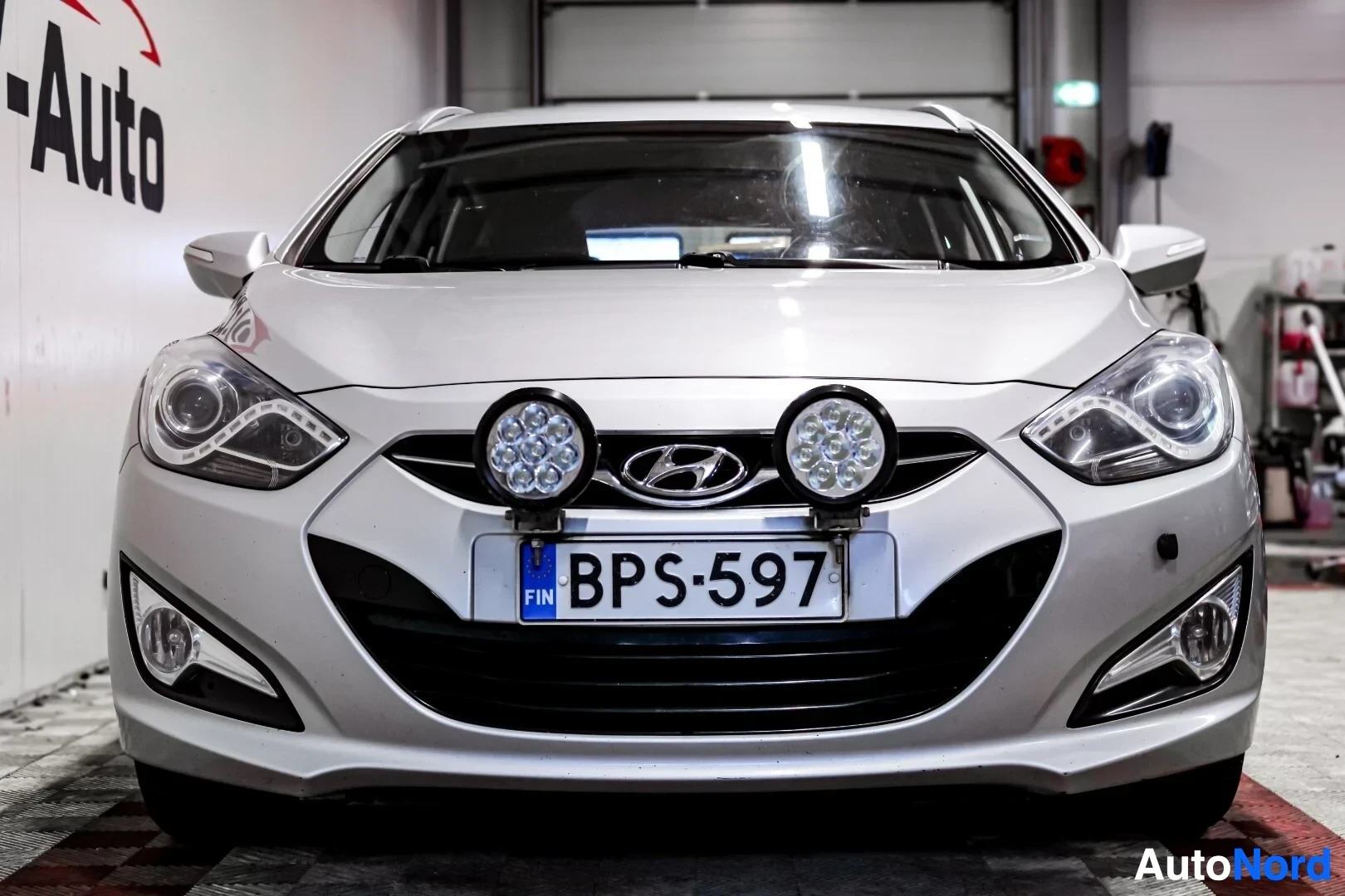 Edestä: Hopeanvärinen Hyundai i40 -farmariauto suoraan edestä kuvattuna. Rekisterikilvessä on tunnus ja sen yläpuolella on kaksi pyöreää lisävaloa