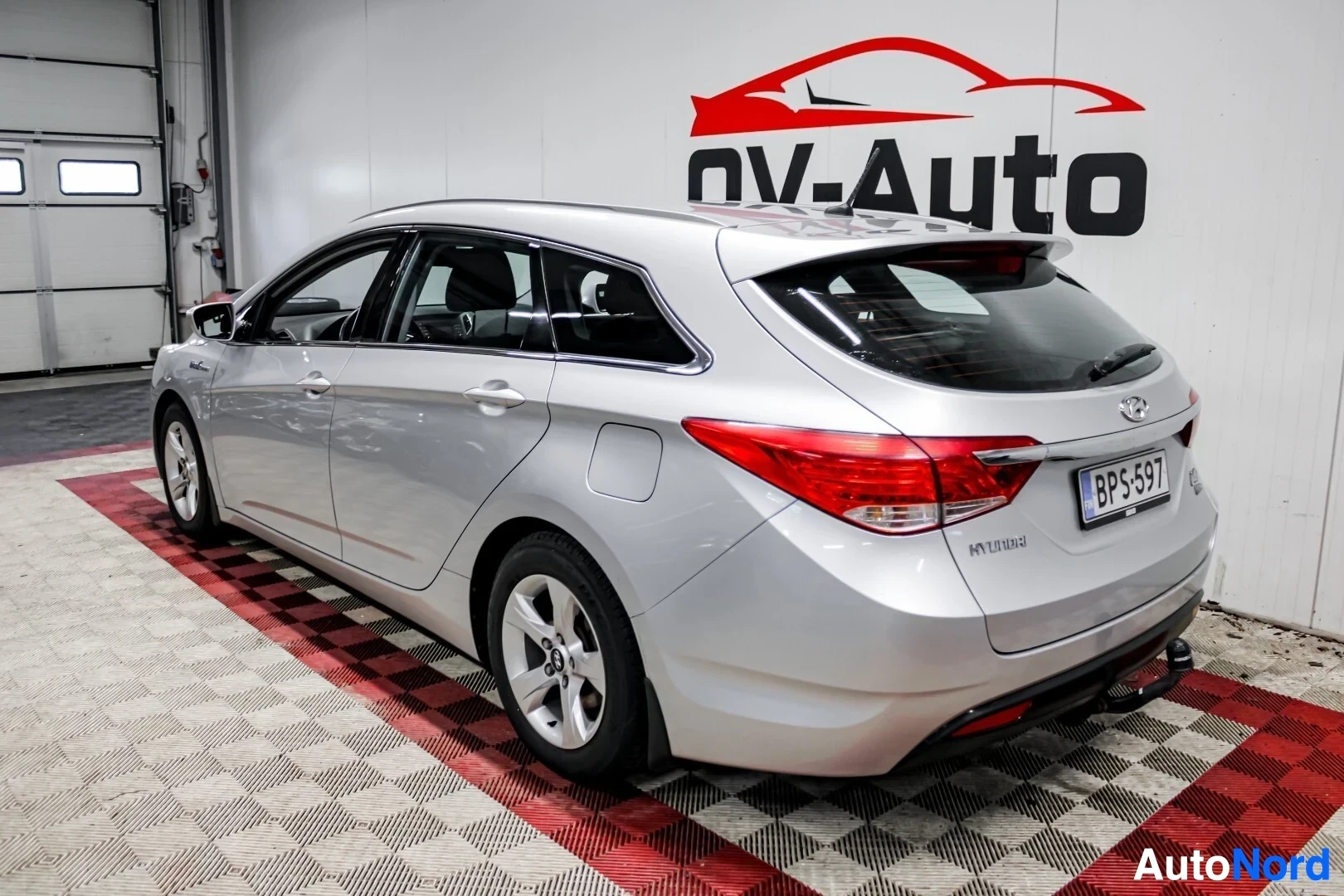Takaviisto: Hopeanvärinen Hyundai i40 -farmariauto kuvattuna takaoikealta sisätilassa. Autossa on kattokiskot ja vetokoukku, sekä rekisterinumero perässä
