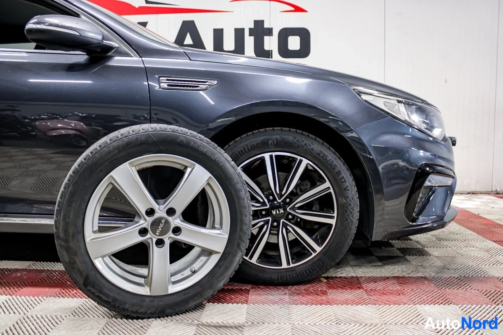 Yksityiskohta: Auton etuosa kuvattuna sivulta päin. Eturenkaan vieressä on erillinen alumiinivanne, jossa on rengas. Auto on harmaa ja siinä on monipuolaiset alumiinivanteet.