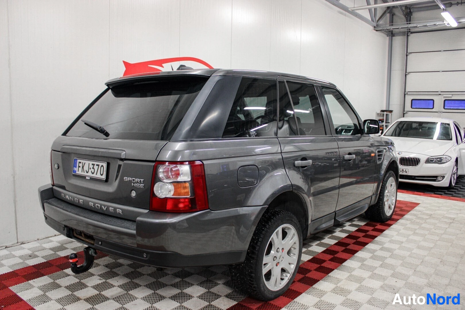 Takaviisto: Harmaa Range Rover Sport, perä ja vasen kylki näkyvissä, sisätiloissa. Perässä näkyy vetokoukku, rekisterikilpi ja takaspoileri