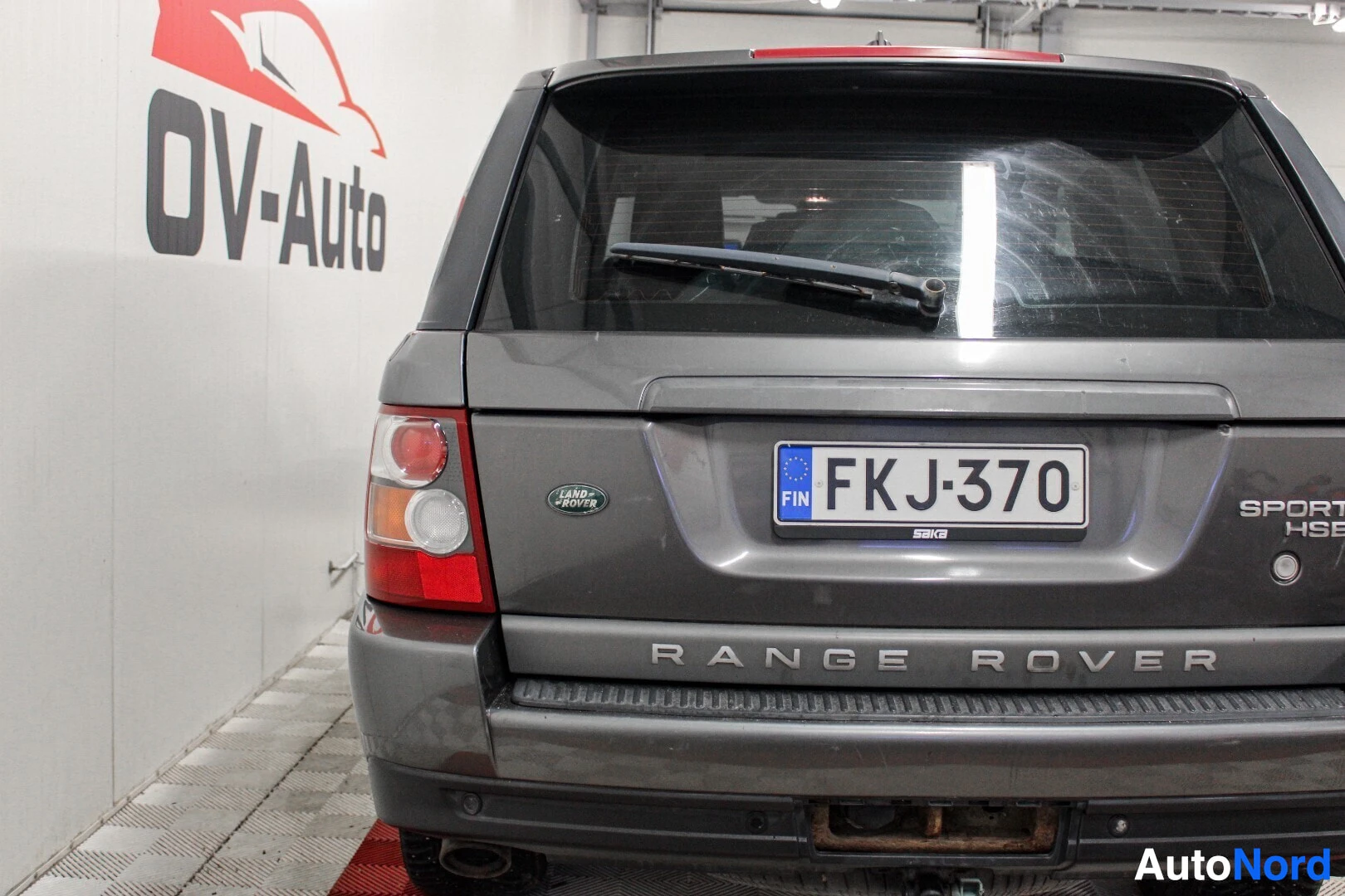 Takaa: Harmaa Range Rover Sportin peräkuva sisätiloissa. Rekisterikilpi on keskellä, takalasissa tuulilasinpyyhin