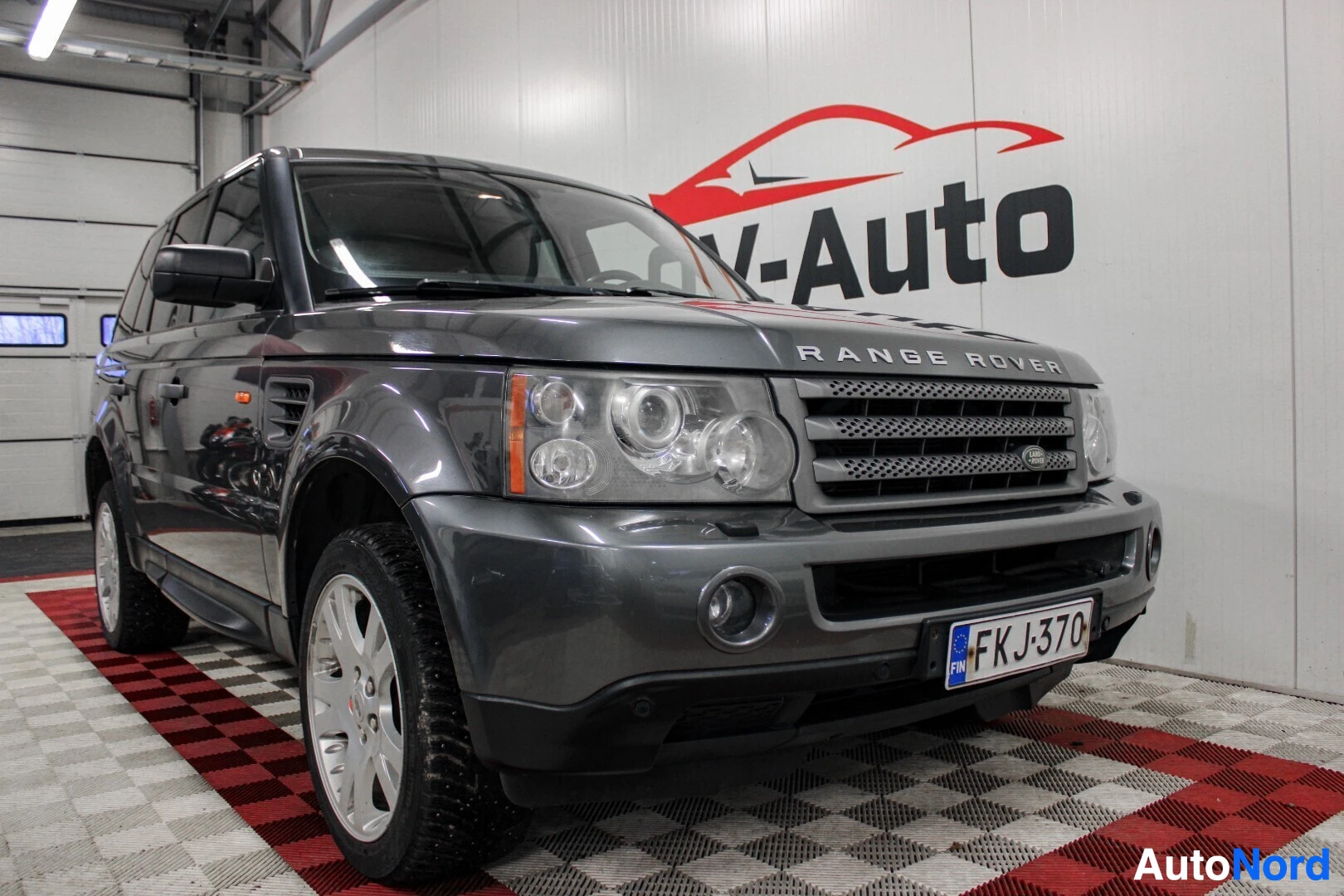 Etuviisto, nokka vasemmalle: Harmaa Range Rover Sportin etupää sisätiloissa, nokka kohti vasenta. Rekisterikilpi näkyy puskurissa