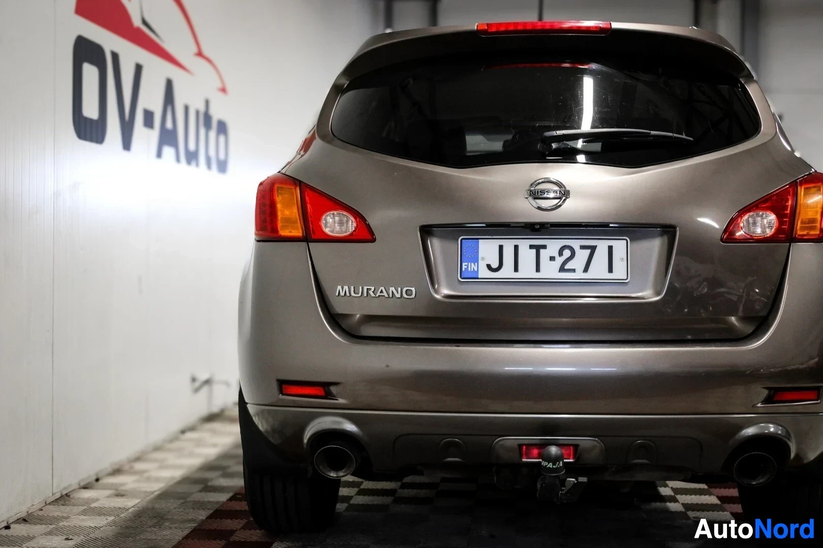 Takaa: Nissan Muranon takaosa kuvattuna matalasta kulmasta. Takaikkunan alla on valkoinen rekisterikilpi, jossa musta teksti "". Takaluukussa on Nissan-logo ja