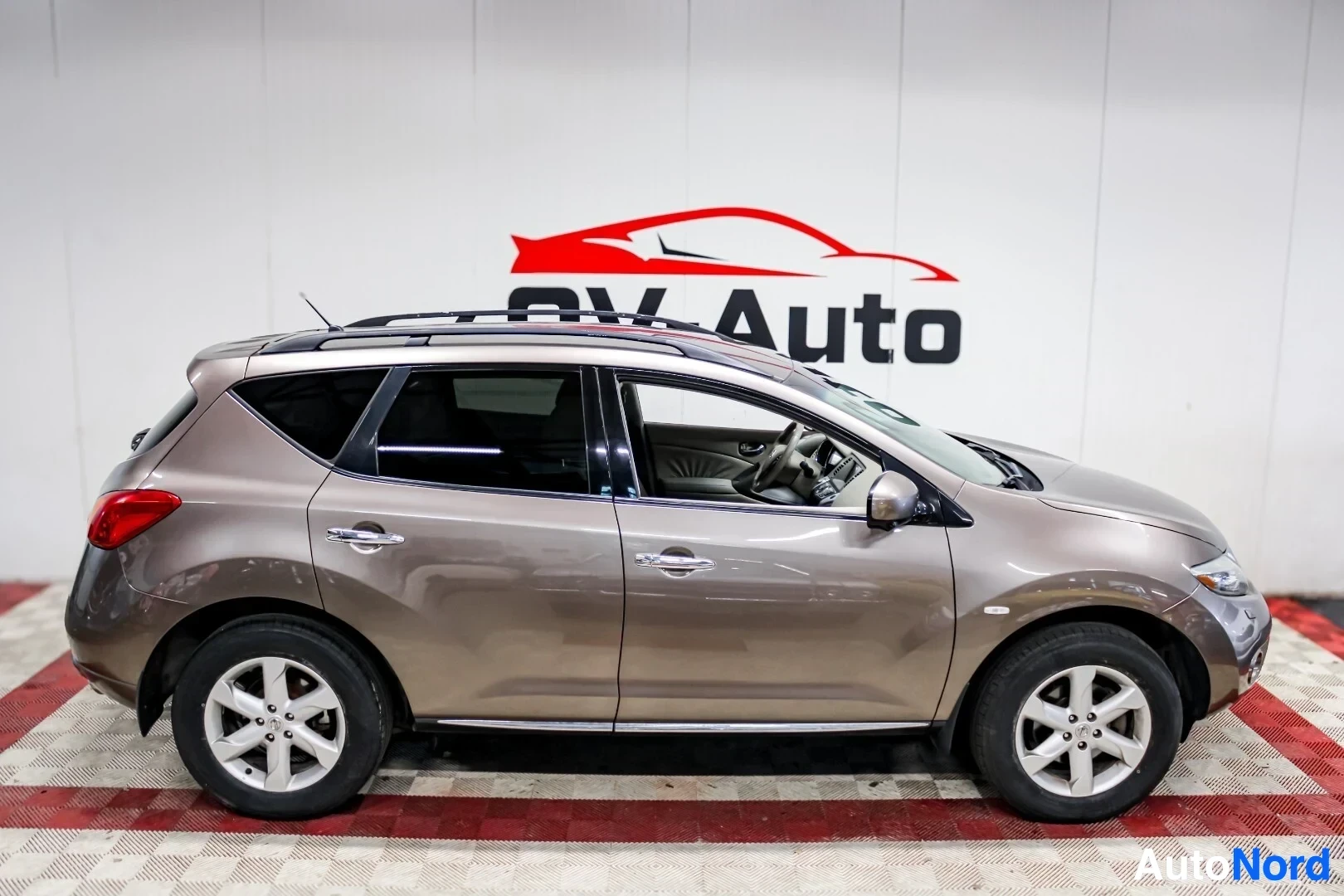 Sivulta: Nissan Murano kuvattuna vasemmalta sivulta. Autossa on kattokaiteet ja hopeanväriset vanteet. Auton väri on vaaleanruskea ja ikkunat ovat tummennetut. Taustalla