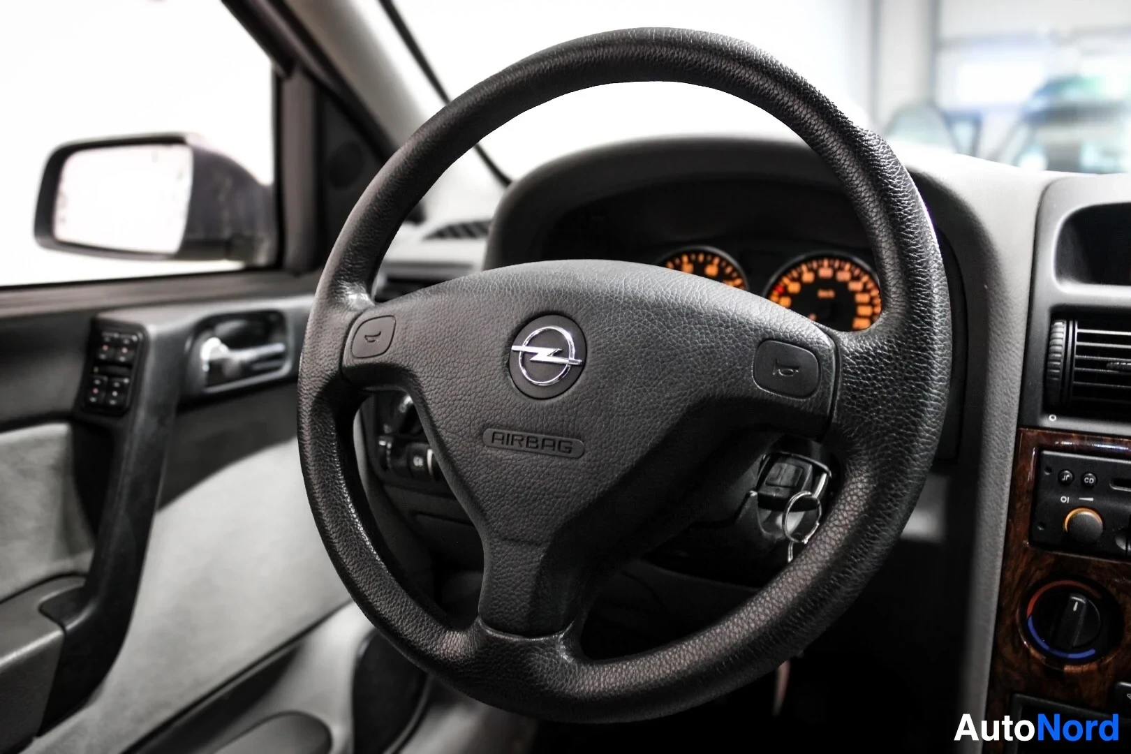 Yksityiskohta: Lähikuva auton ohjauspyörästä, jossa on Opel-logo ja 'AIRBAG'-merkintä. Taustalla näkyy osittain mittaristo ja oikealla keskikonsolin yläosa.