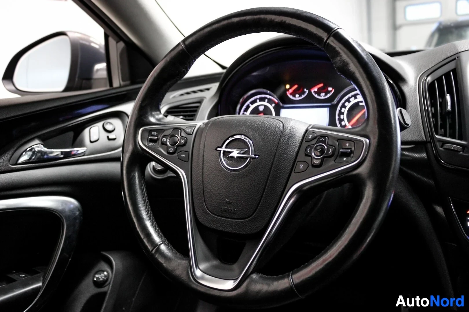 Yksityiskohta: Lähikuva auton mustasta, monitoimiohjauspyörästä, jossa on hopeisia yksityiskohtia ja Opel-logo keskellä. Taustalla näkyy mittaristo.