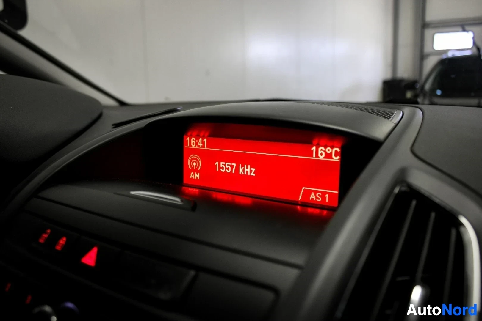 Yksityiskohta: Lähikuva ajoneuvon keskikonsolin näytöstä, jossa lukee "16:41", "1557 kHz" ja "16°C".