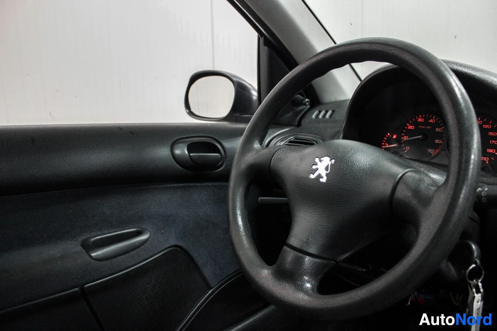 Yksityiskohta: Sisäkuva ohjauspyörästä ja kuljettajan oven sisäpaneelista. Peugeotin logo on näkyvissä ohjauspyörän keskellä.