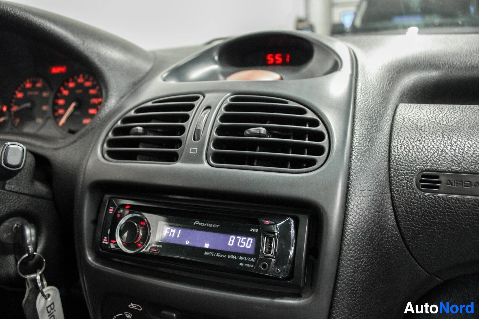 Yksityiskohta: Lähikuva auton keskikonsolista, jossa näkyy ilmanvaihtoaukot ja Pioneer-merkkinen autoradio. Radion näytöllä lukee "FM1" ja "87.50". Takanäytöllä lukee "551".