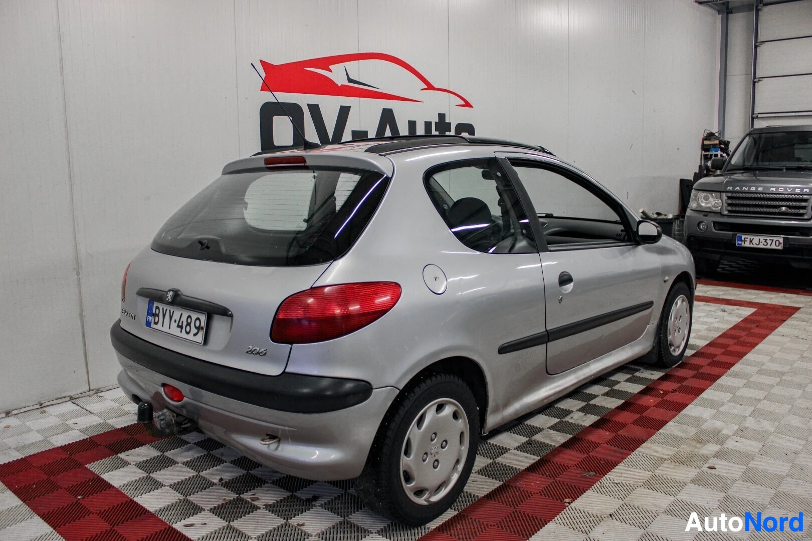 Takaviisto: Hopeinen Peugeot 206 viistosti takavasemmalta kuvattuna. Auton takaluukussa näkyy rekisterikilpi ja vetokoukku