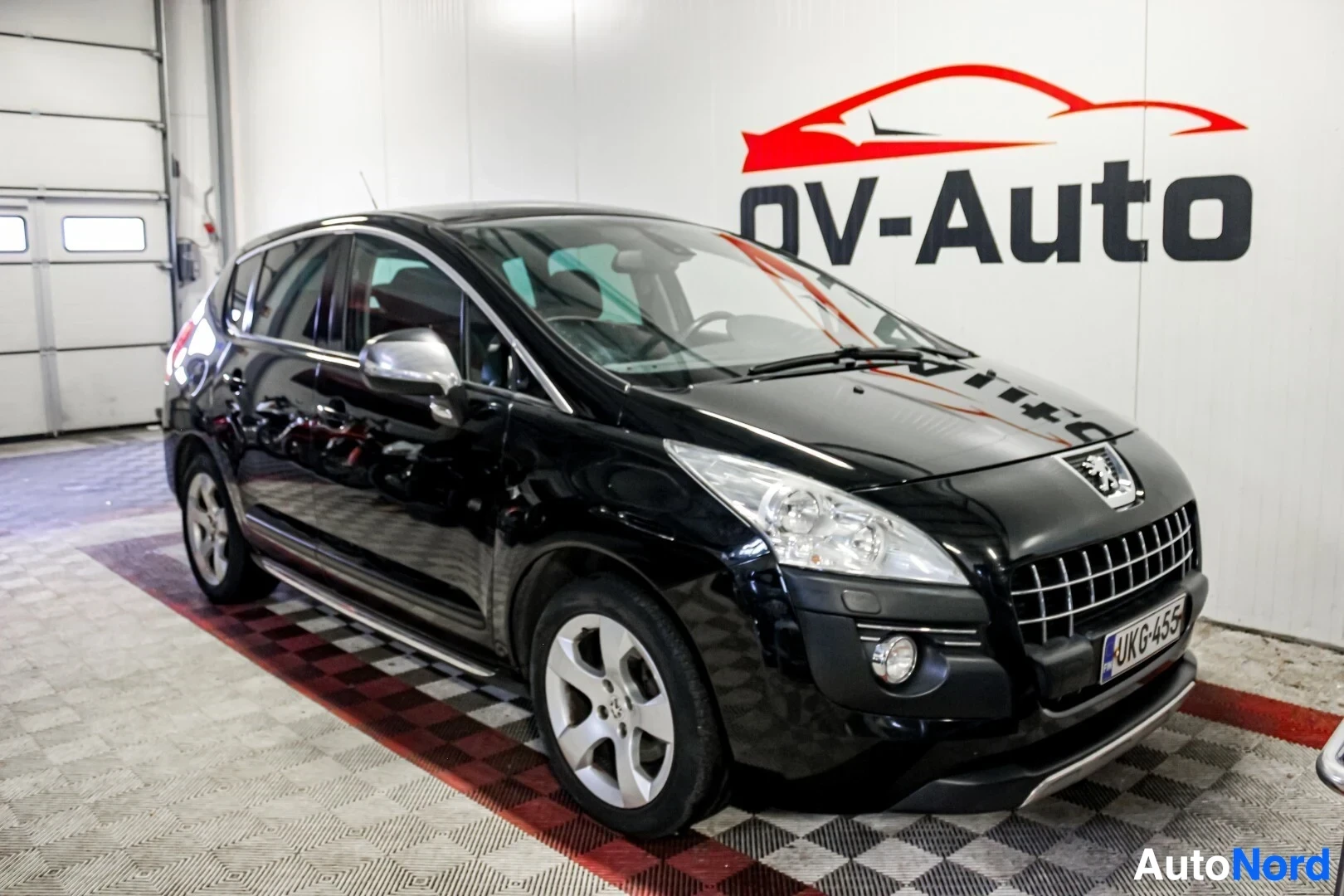 Etuviisto, nokka oikealle: Musta Peugeot 3008 etuvasemmalta kuvattuna sisätiloissa. Auton rekisterinumero on. Autossa on viisipuolaiset kevytmetallivanteet ja kattokiskot