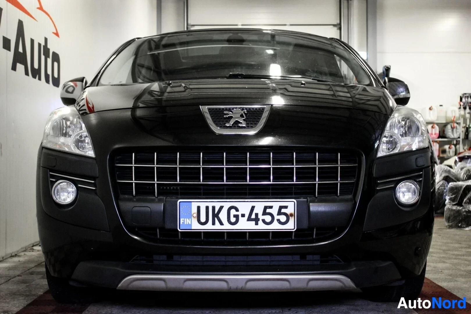 Edestä: Musta Peugeot 3008 edestä päin kuvattuna sisätiloissa. Auton rekisterinumero on. Ajovalot ja etusumuvalot ovat näkyvissä