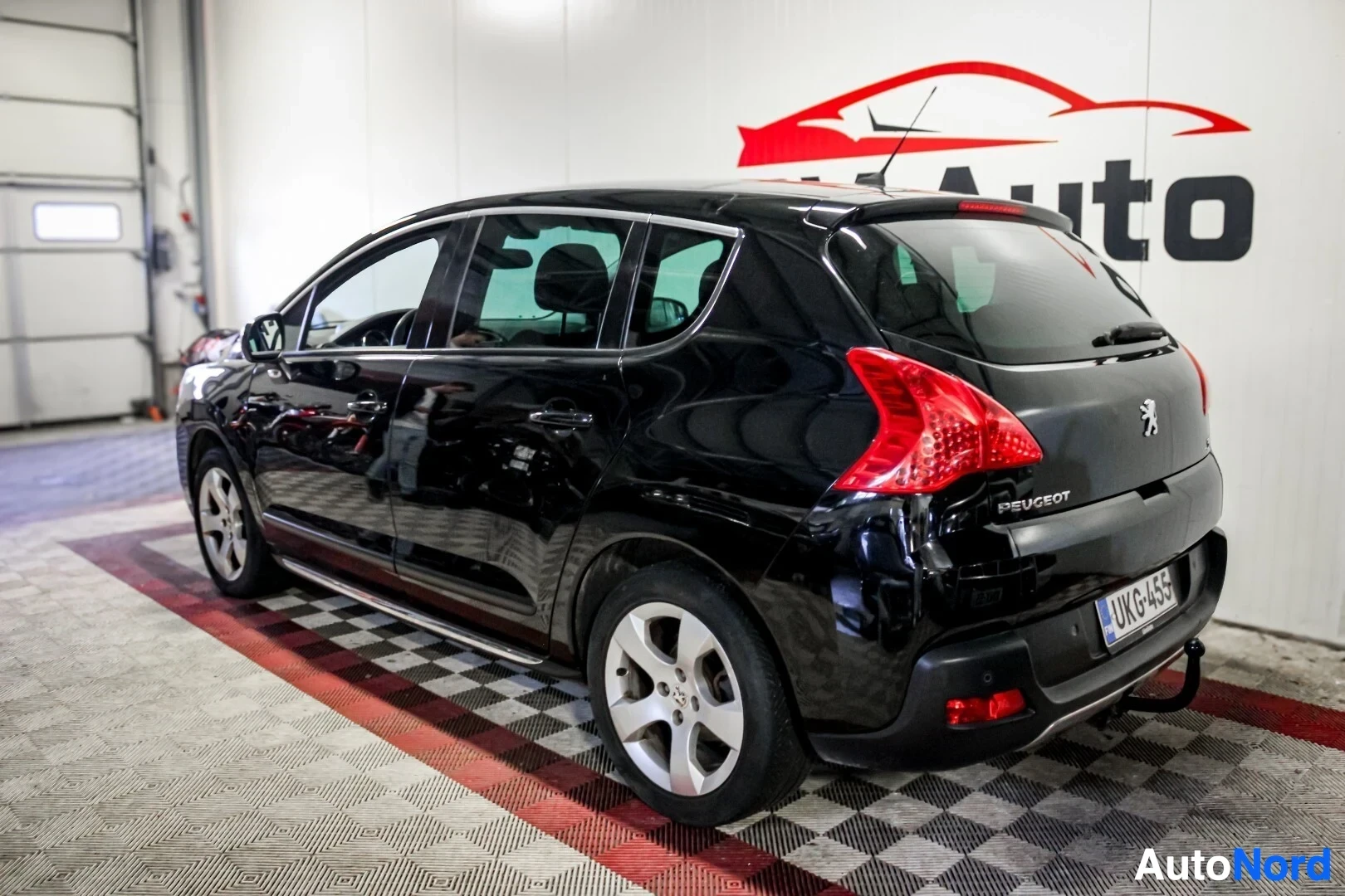 Takaviisto: Musta Peugeot 3008 takavasemmalta kuvattuna sisätiloissa. Auton rekisterinumero on. Autossa on viisipuolaiset kevytmetallivanteet ja kattokiskot