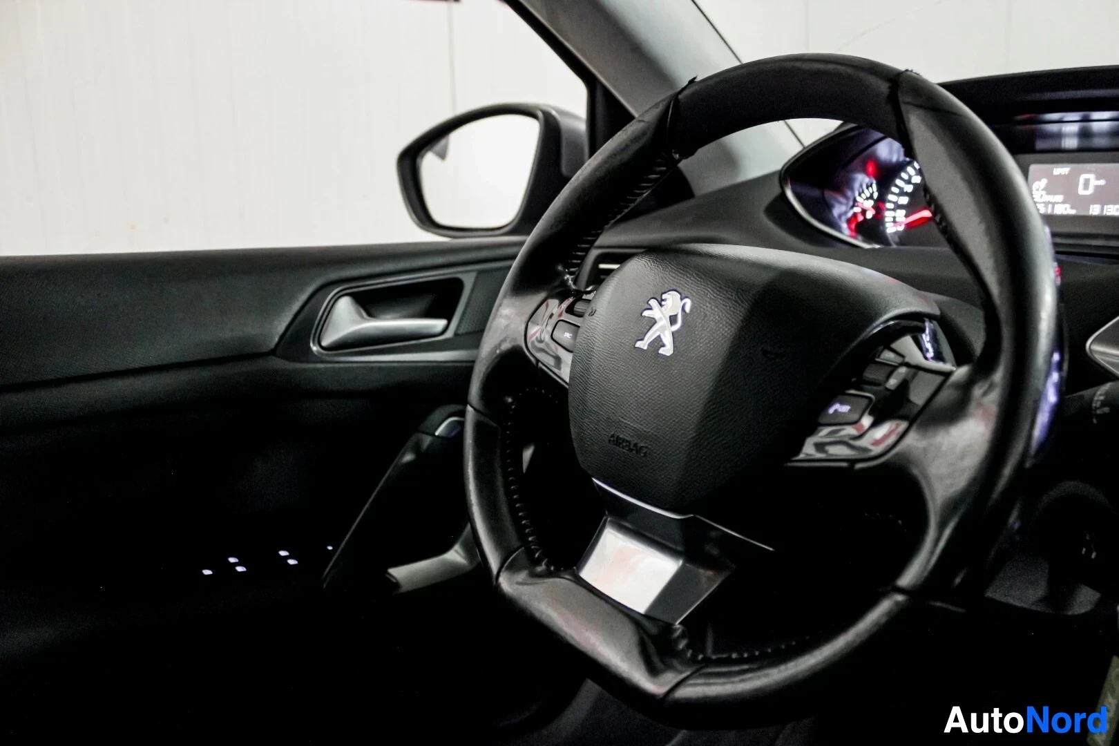 Ohjaamo: Musta monitoimiohjauspyörä ja mittaristo näkyvissä kuljettajan paikalta kuvattuna. Keskellä ohjauspyörää on Peugeot-logo ja teksti "AIRBAG".