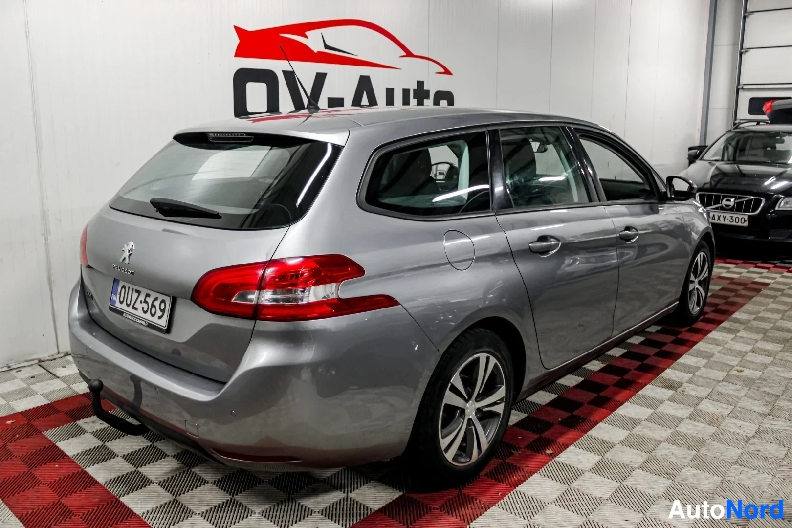 Takaviisto: Hopeanvärinen Peugeot 308 -farmariauto kuvattuna takaviistosta oikealta sisätiloissa. Autossa on kattokiskot, vetokoukku ja monipuolaiset kevytmetallivanteet. R