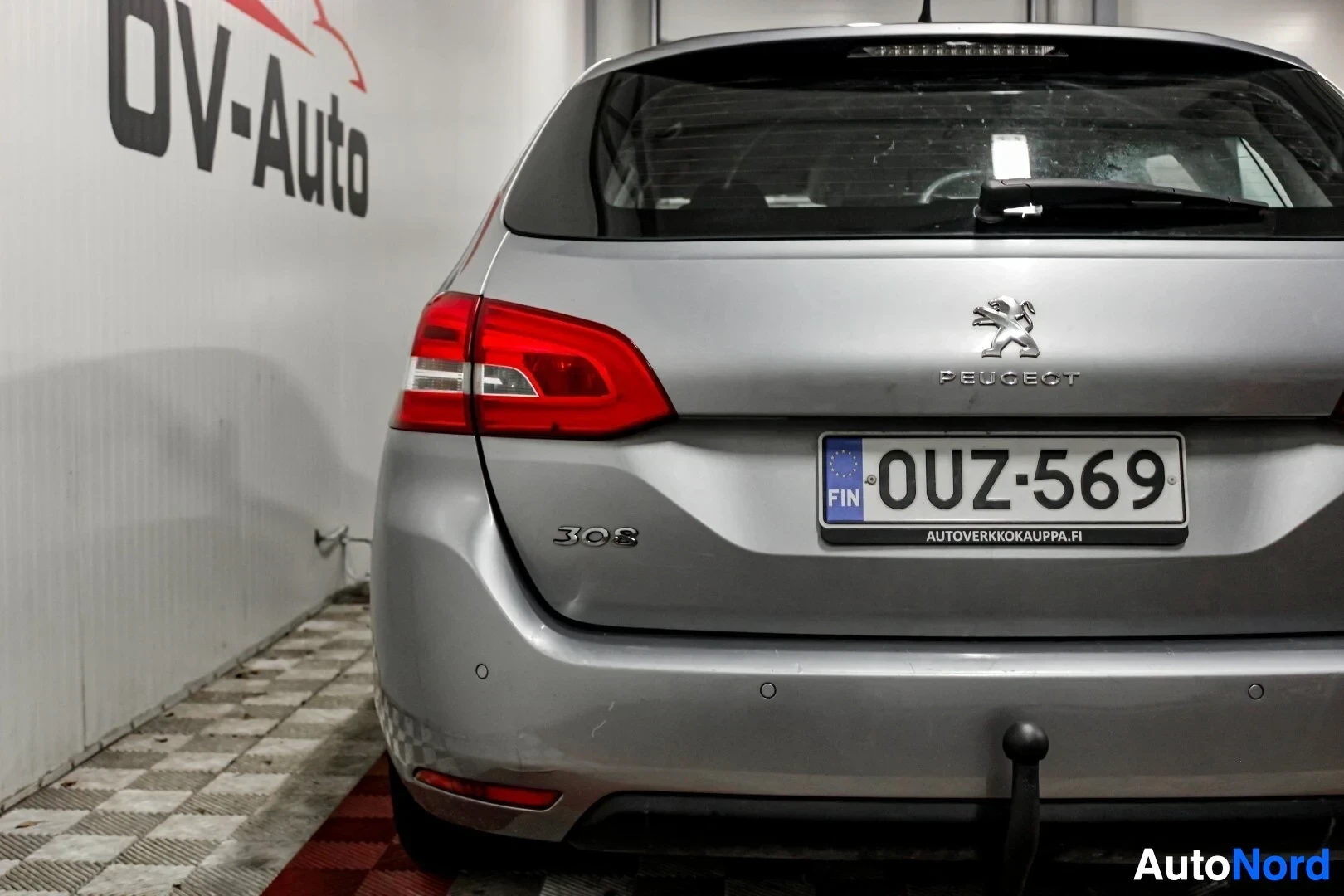 Takaa: Peugeot 308 -farmariauton perä, jossa rekisterikilpi "", näkyvissä lähemmin. Autossa on vetokoukku ja pysäköintitutka-anturit takapuskurissa. Takavalot j