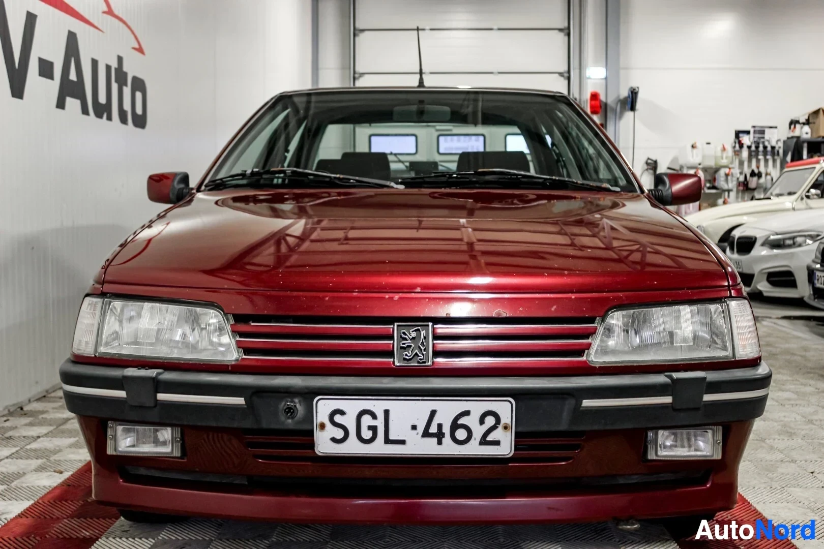 Edestä: Punaisen Peugeot 405:n etuosa kuvattuna suoraan edestä autokaupan sisätiloissa. Auton rekisterikilpi on
