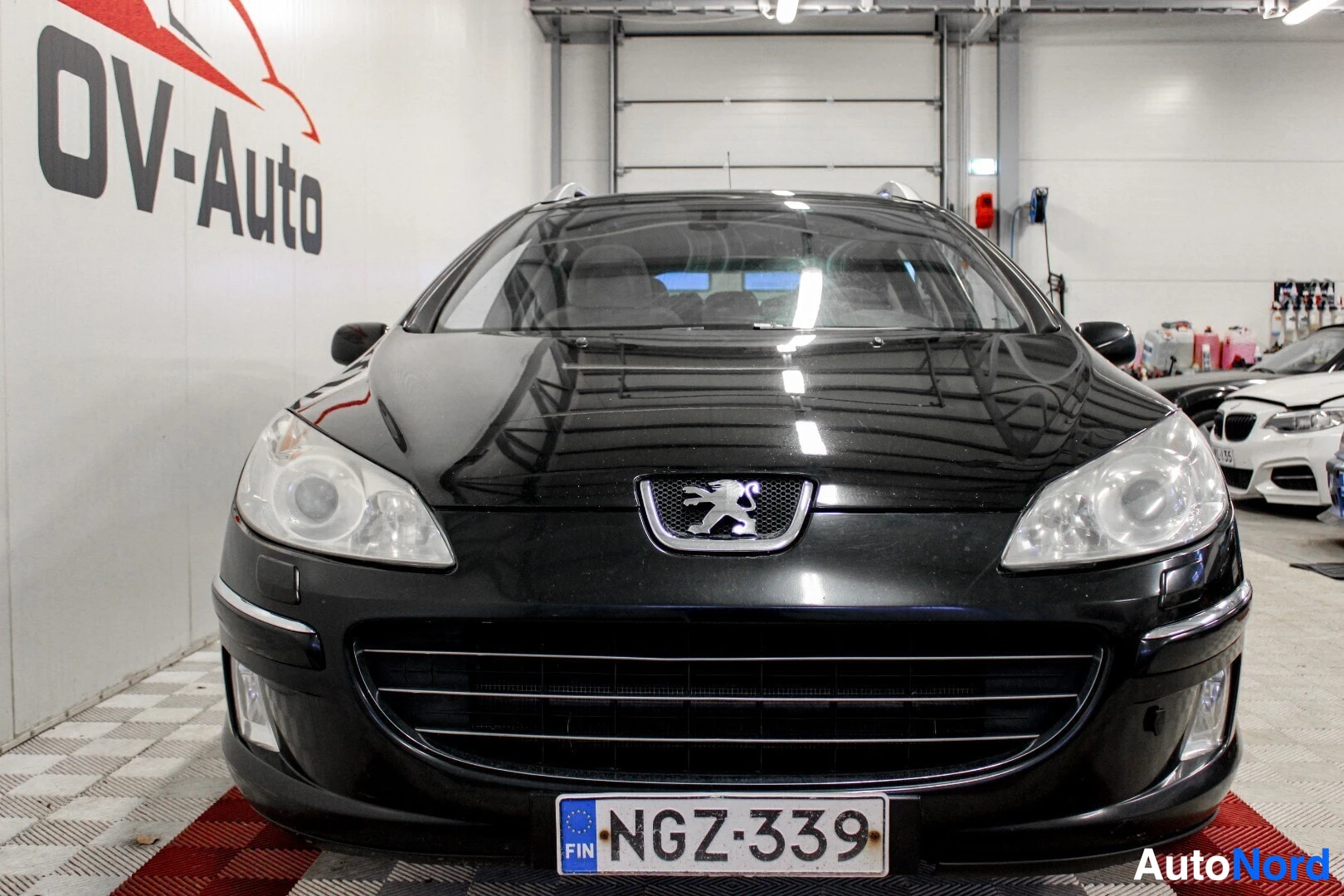 Edestä: Mustan Peugeot 407 SW:n etuosa kuvattuna suoraan edestä. Etusäleikkö ja ajovalot ovat keskiössä.
