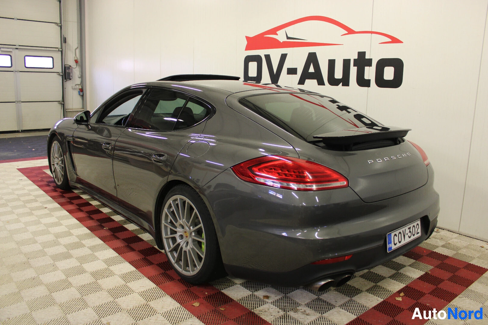 Takaviisto: Tummanharmaa Porsche Panamera S 3.0 V6 e-Hybrid takaa ja oikealta sivulta kuvattuna sisätiloissa. Autossa on kattoluukku, takaspoileri ja hopeiset monipuolavant