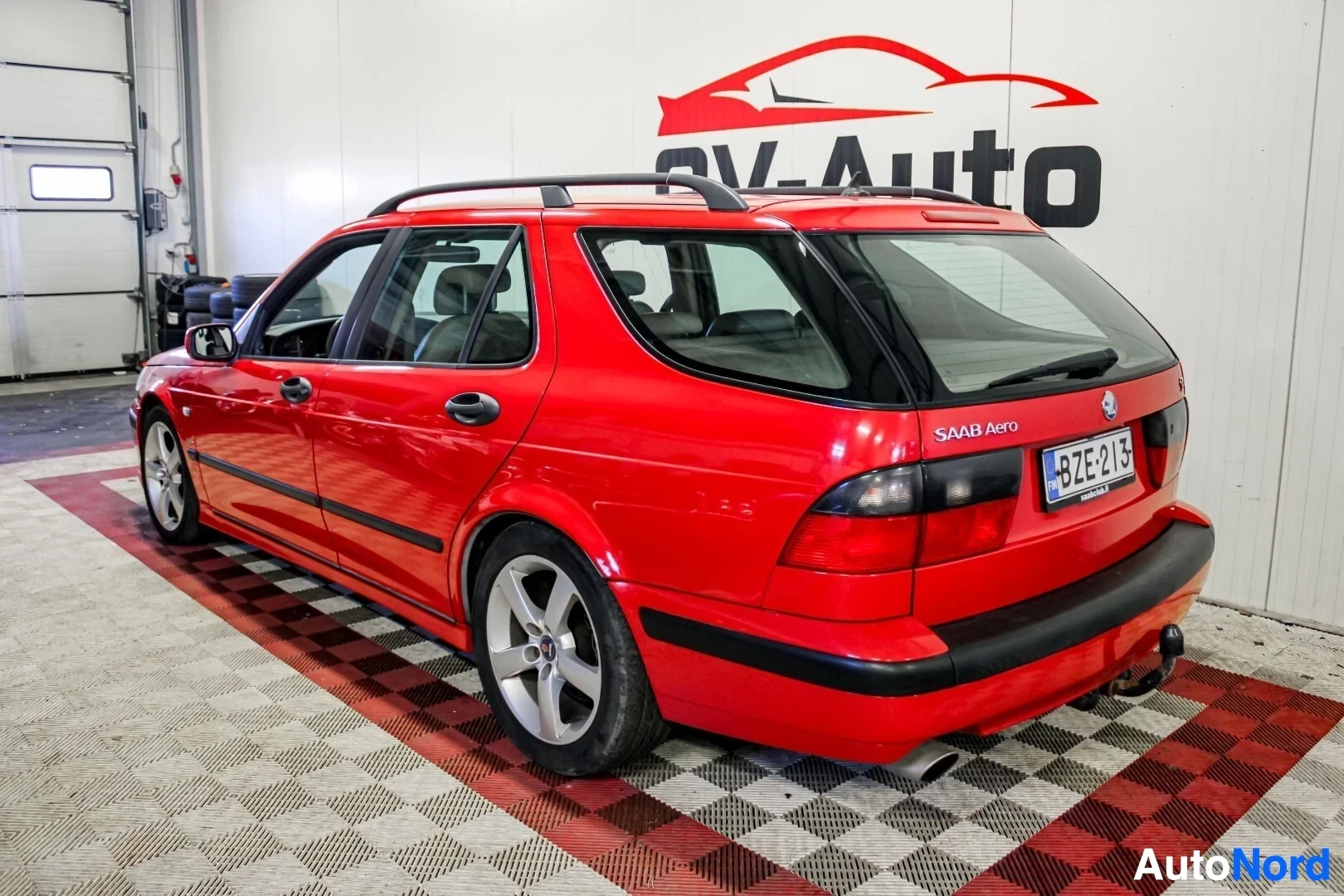 Takaviisto: Punainen farmariauto takaa ja oikealta sivulta kuvattuna sisätiloissa. Autossa on kattokaiteet, vetokoukku ja kevytmetallivanteet.