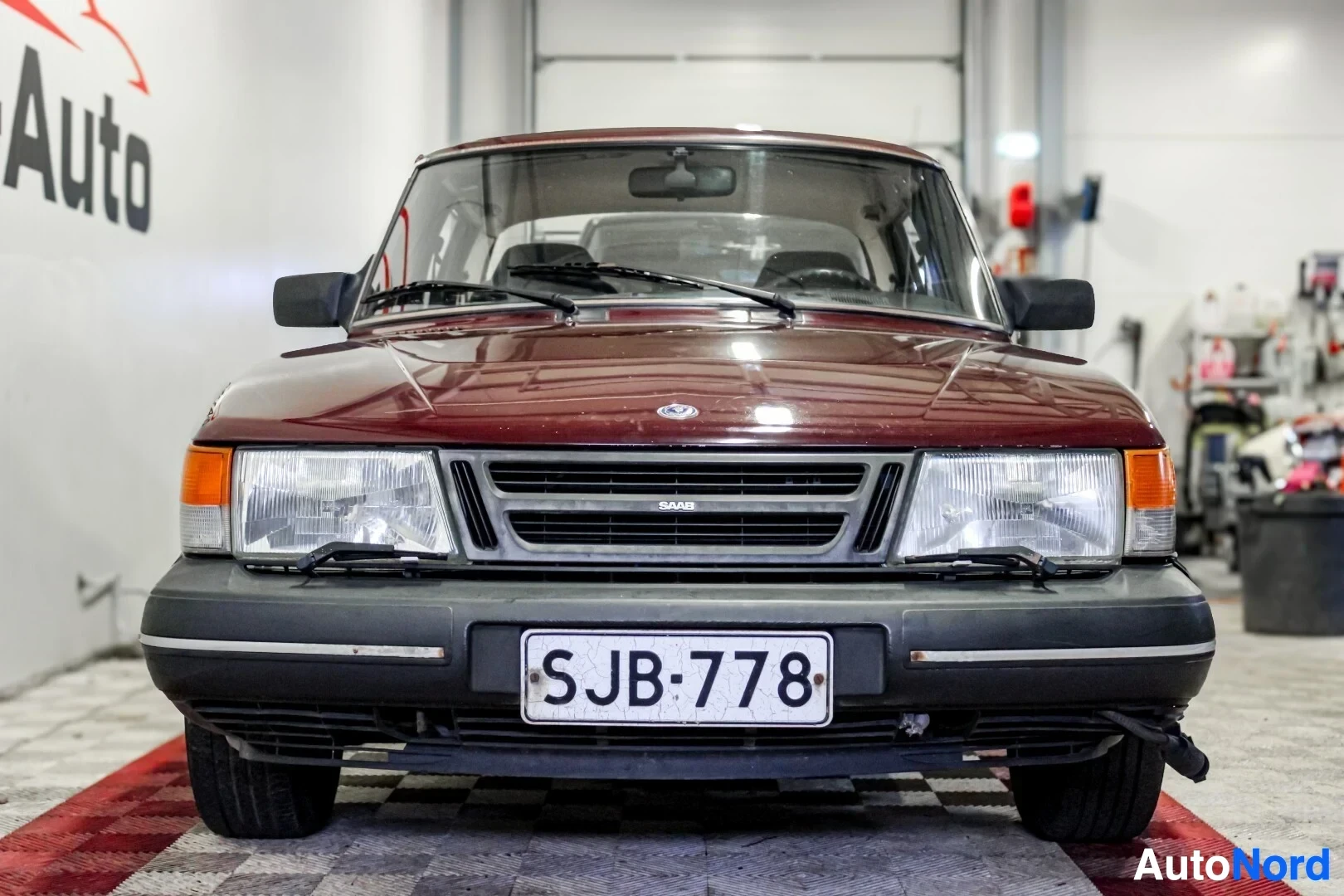 Edestä: Saab 900 -henkilöauton etuosa, rekisteritunnus, edestä kuvattuna OV-Auto -kyltin edessä sisätiloissa