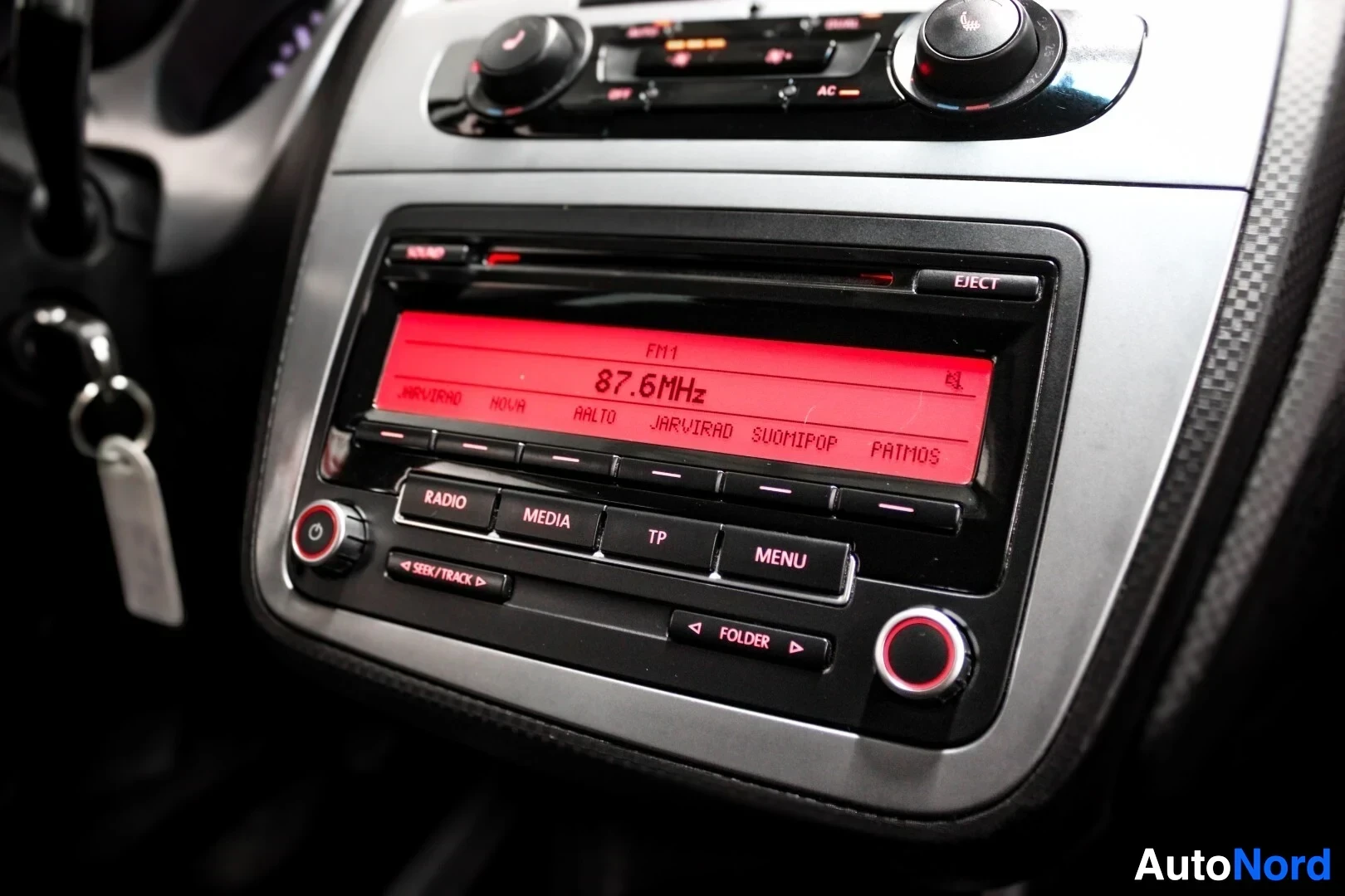 Yksityiskohta: Lähikuva auton radiosta ja ohjauspaneelista. Radion näytössä lukee "87.6 MHz".