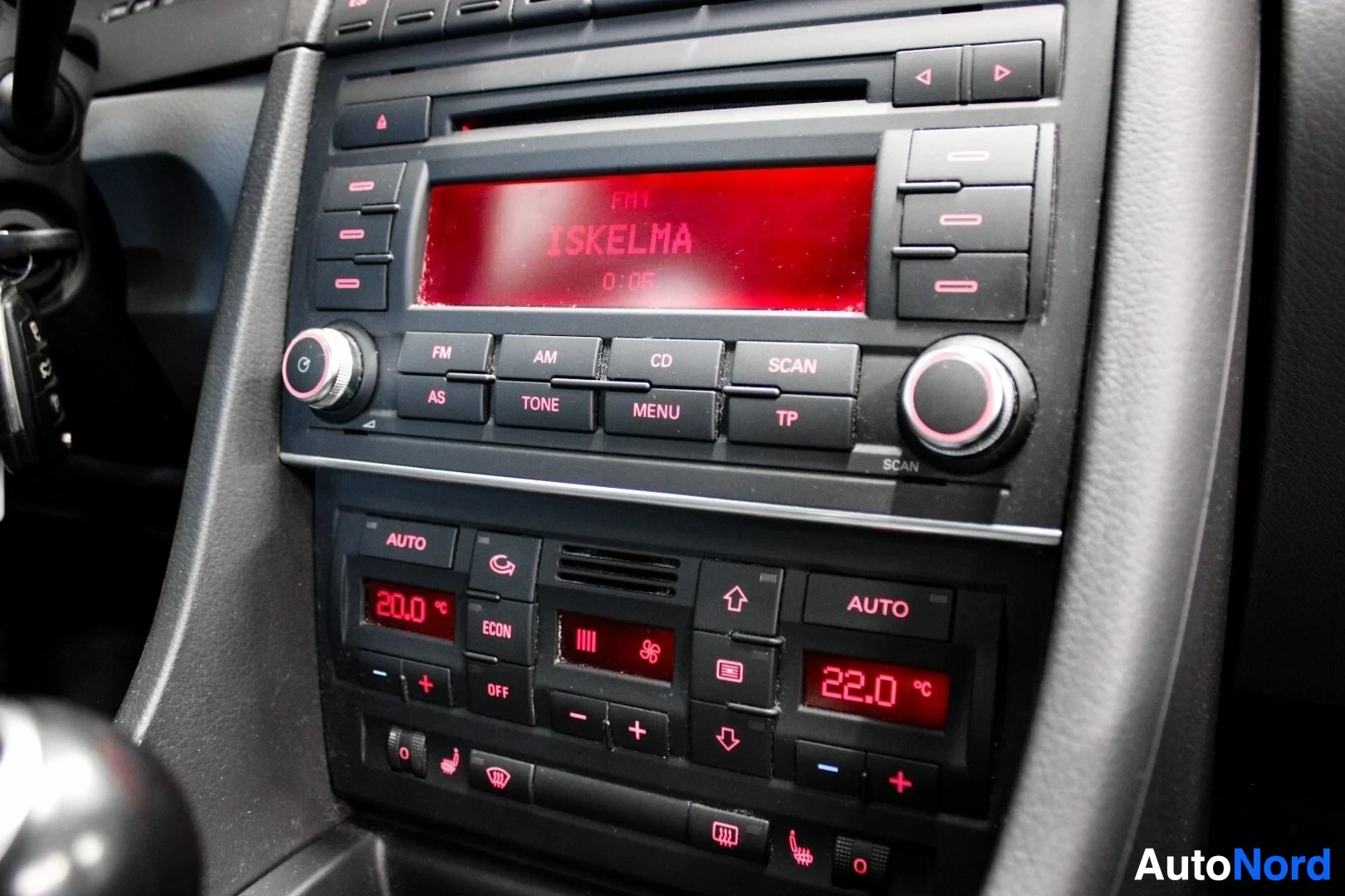 Yksityiskohta: Lähikuva keskikonsolin radiosta ja ilmastoinnin säätimistä. Radionäytöllä lukee "FM1 ISKELMA 0:05" ja ilmastoinnin näytöissä "20.0" ja "22.0".