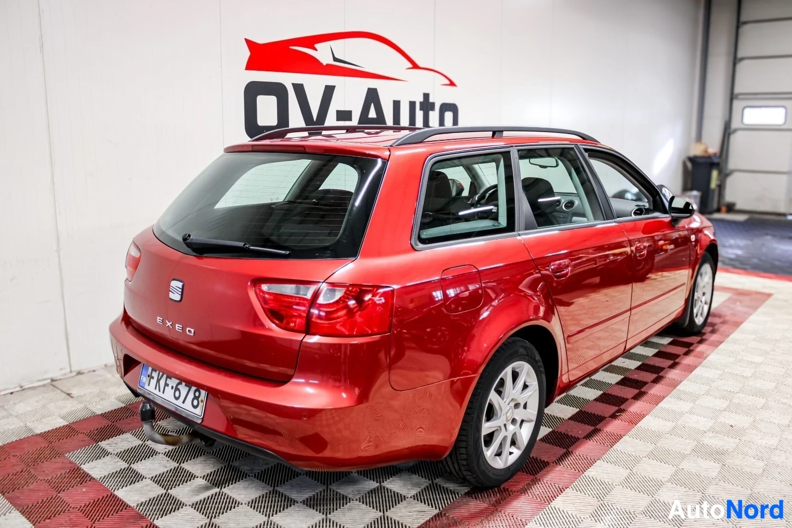 Takaviisto: Punainen farmariauto kuvattuna takavasemmalta. Autossa on kattokaiteet ja vetokoukku. Takana on rekisterikilpi ""