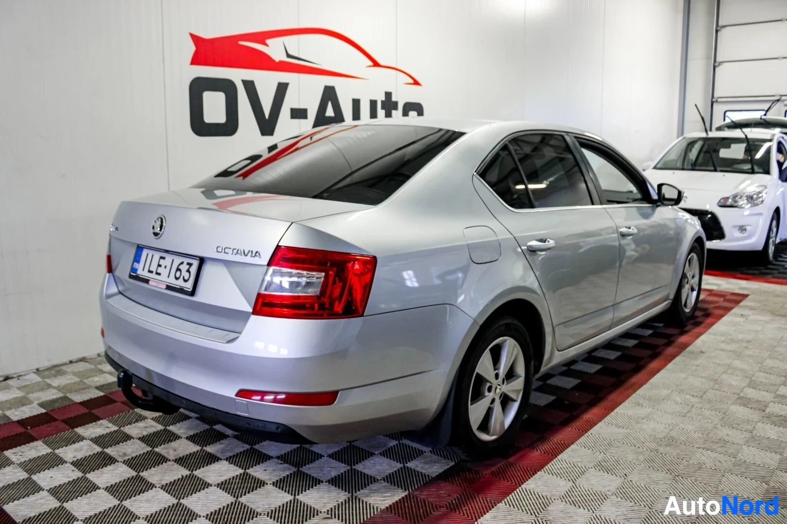 Takaviisto: Hopeanvärinen Skoda Octavia vasemmasta takaviistosta kuvattuna. Autossa on peräkoukku ja metallivanteet.