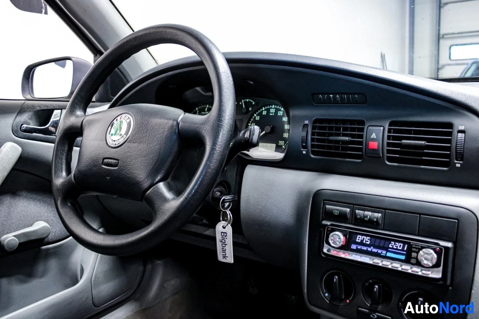 Ohjaamo: Kuvassa näkyy auton ohjaamo, jossa on musta kolmipuolainen ohjauspyörä Skoda-logolla ja mittaristo, jossa näkyy nopeusmittari ja kierroslukumittari. Kojelaudass