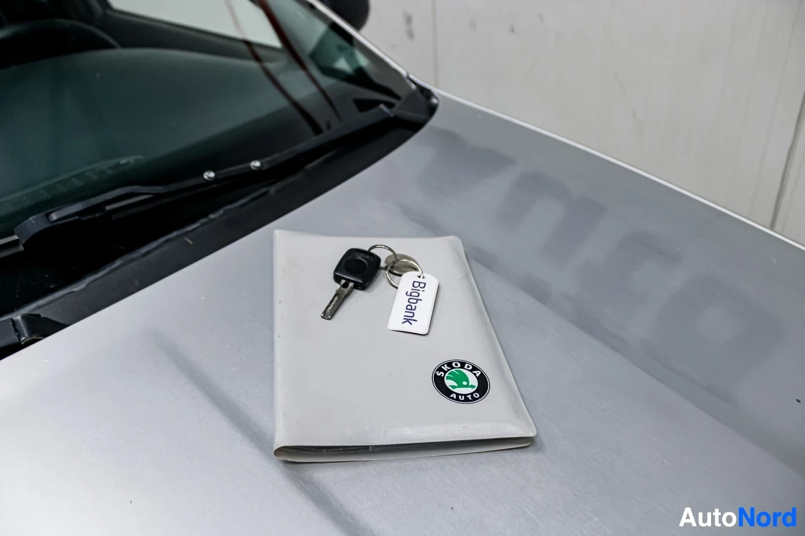 Yksityiskohta: Avaimet ja harmaa kotelo, jossa on Skoda Auto -logo, auton konepellillä.