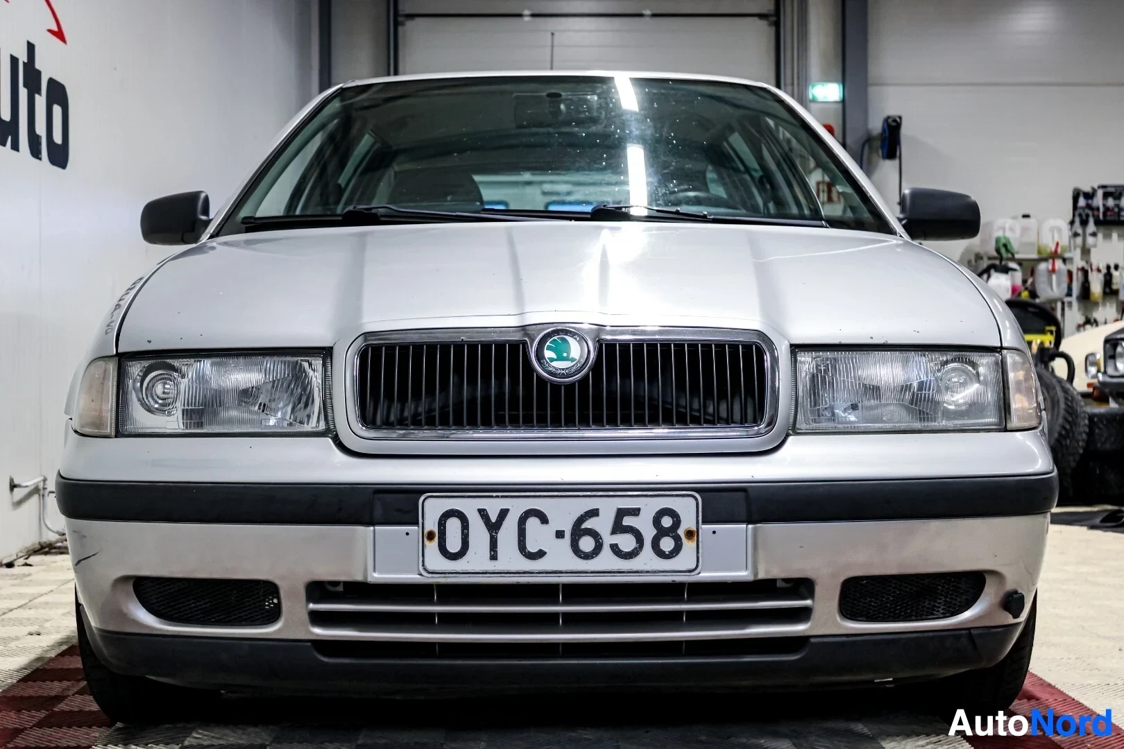 Edestä: Hopeanvärisen Skoda Octavia Combi -henkilöauton etuosa, jossa on musta säleikkö ja ajovalot, sekä rekisterikilpi tekstillä. Keulan alaosassa on kaksi il