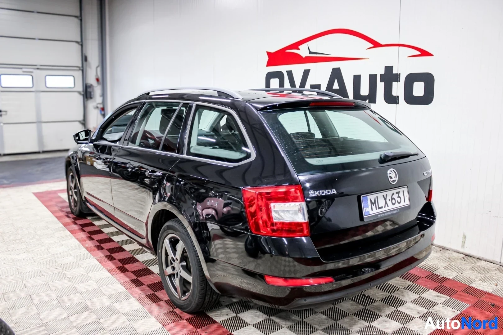 Takaviisto: Musta Skoda Octavia Combi pysäköitynä viistosti vasemmalle takaviistosta kuvattuna, takavalot ja takaluukku näkyvissä. Kattokaiteet ja takaikkunoiden tummennuks